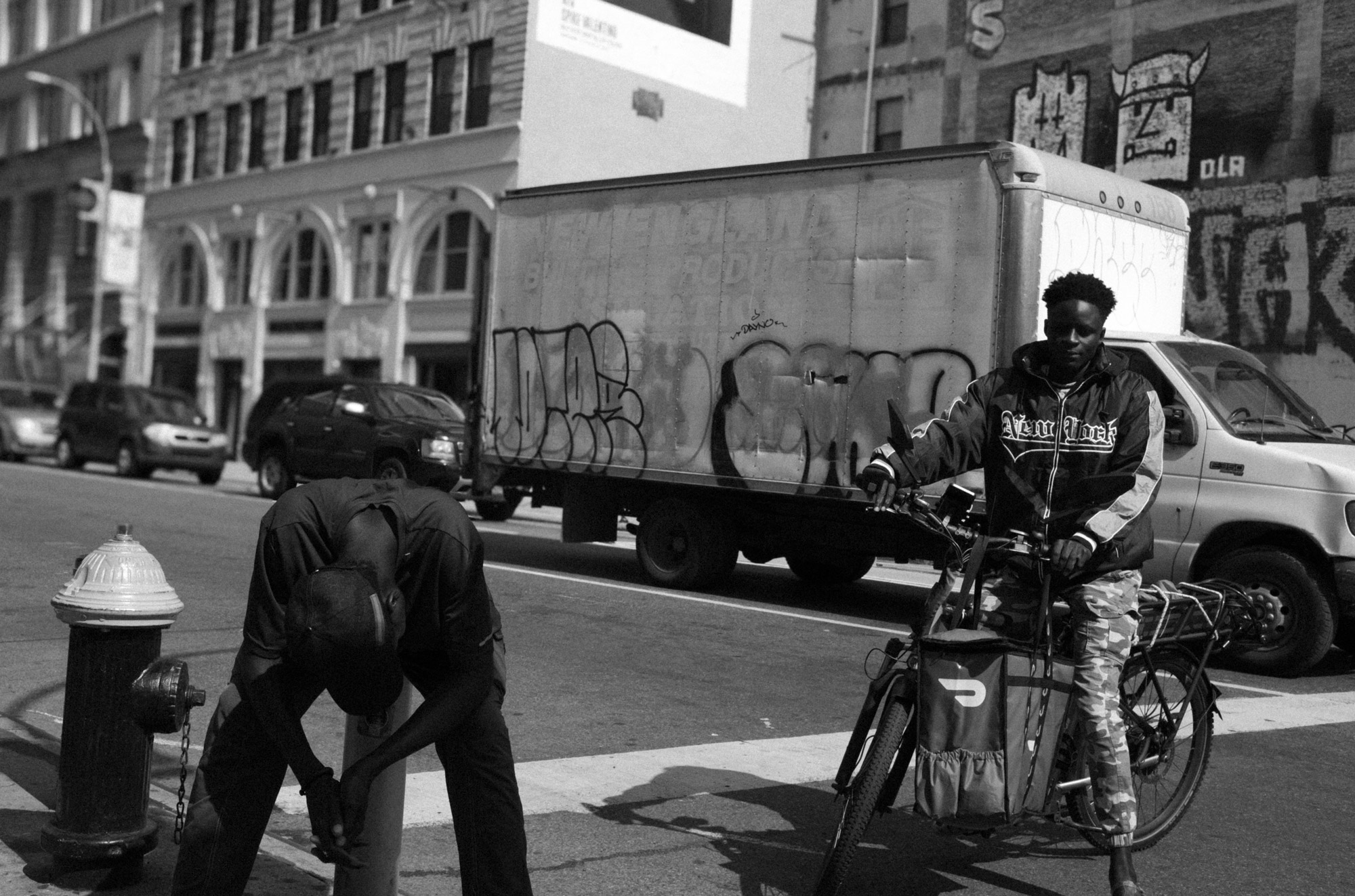 A black-and-white photo of a person on a bicycle and a person sitting on a New York City street