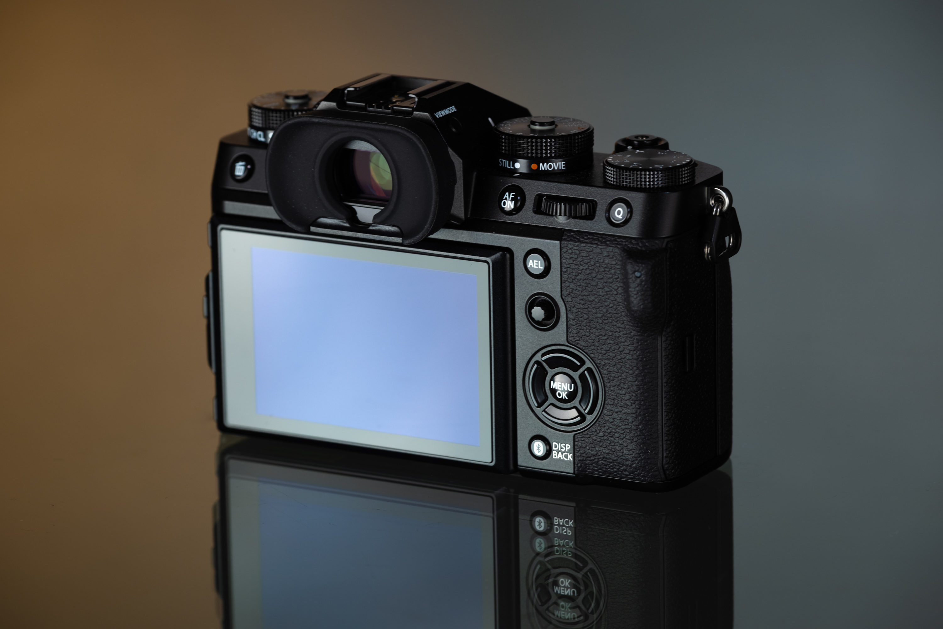 L'écran LCD arrière d'un Fujifilm X-T5 se reflète sur une table en verre sur un fond orange et gris.