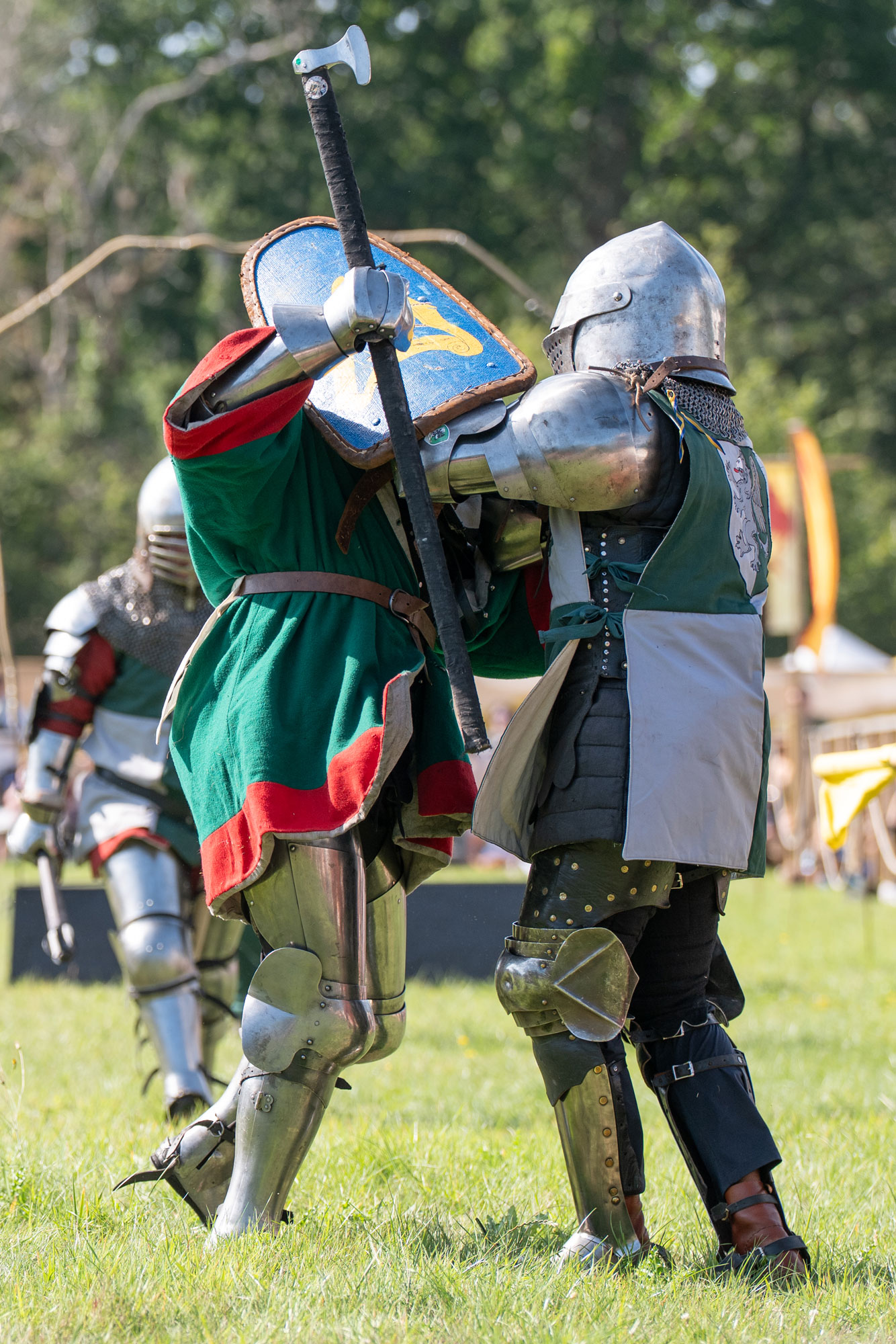 Two people in knight’s costumes, one holding a shield, another holding an axe, clash in a staged battle.