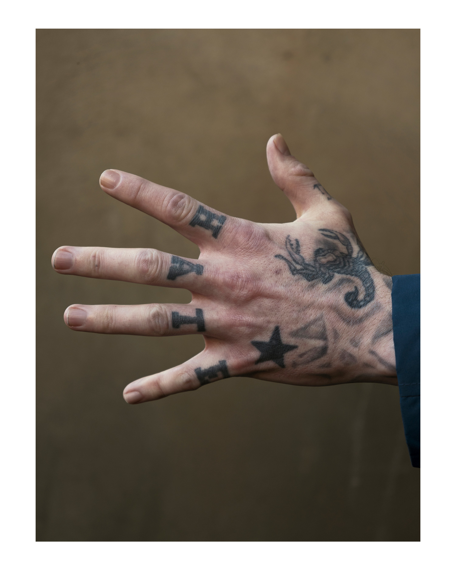 A hand with tattoos spelling out ‘Hate’ on the fingers, held out in front of a wall, photo by Simon Murphy with the Fujifilm GFX 50S