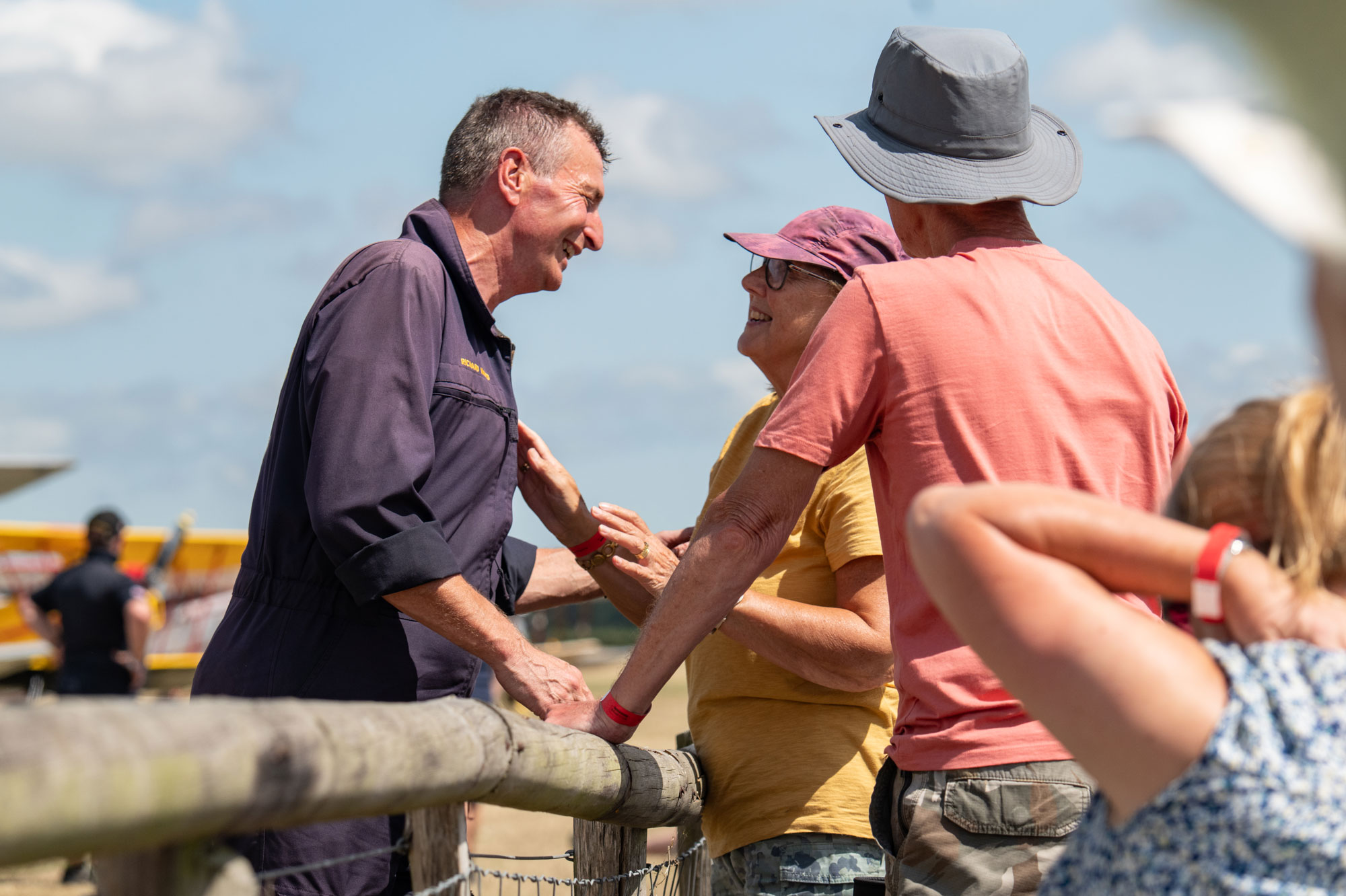 A person in a flying jacket greets their family, talking over a fence at waist height, photo by Amy Moore with the Panasonic S1R II.