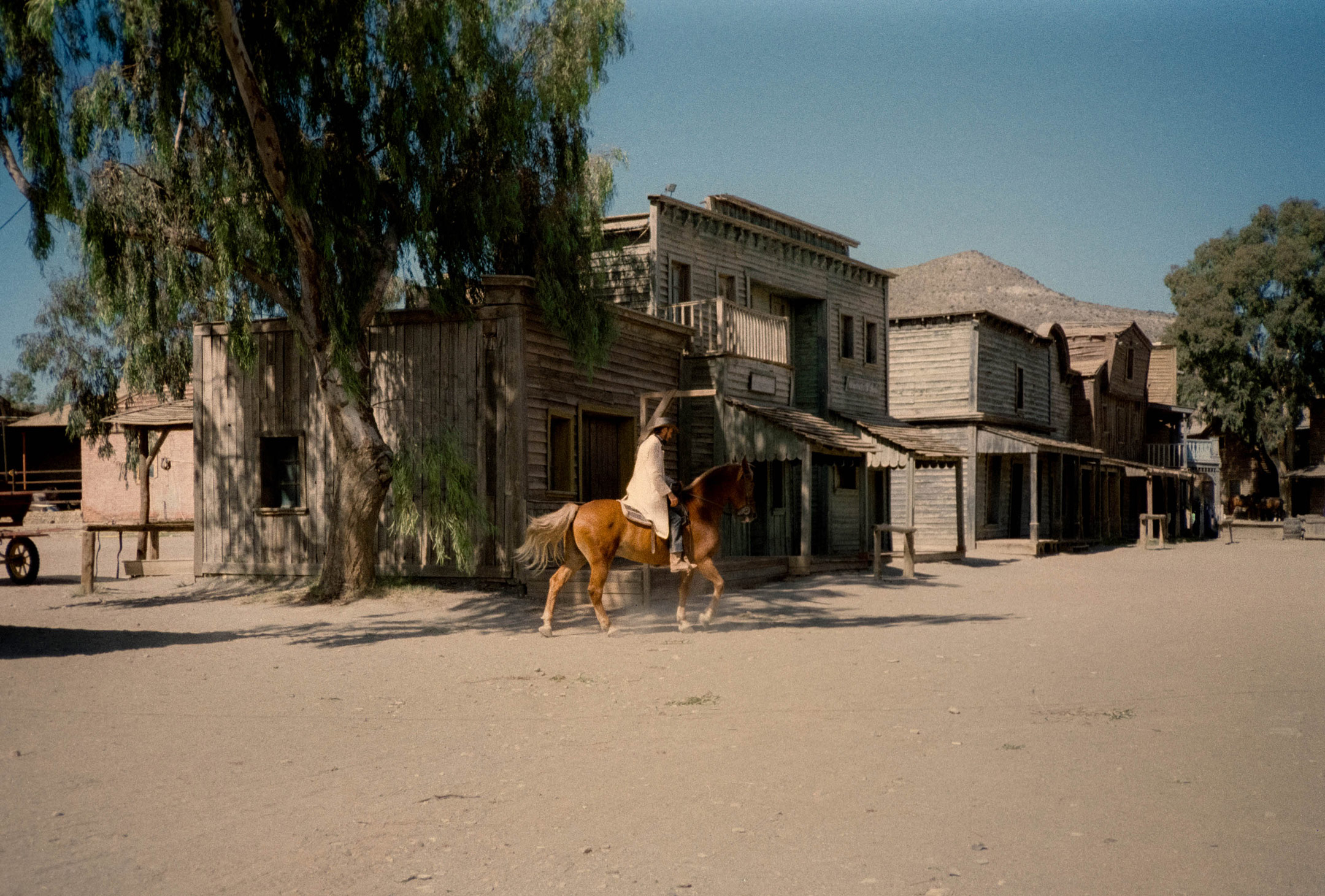 A person riding a horse in a western looking town by Ian Howorth