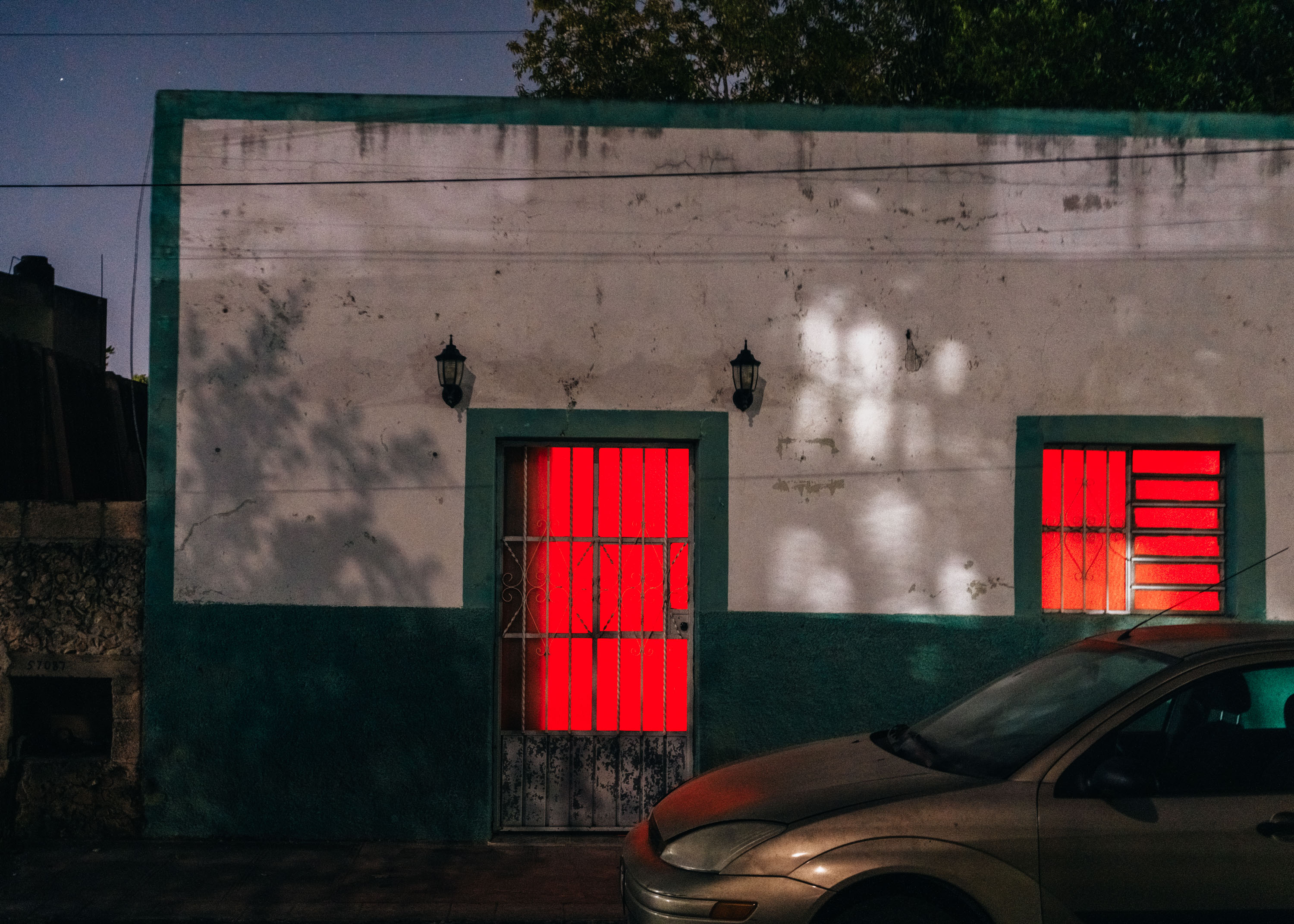 A building in Mexico with red glowing lights in the windows creating an eerie atmosphere. By Ian Howorth.