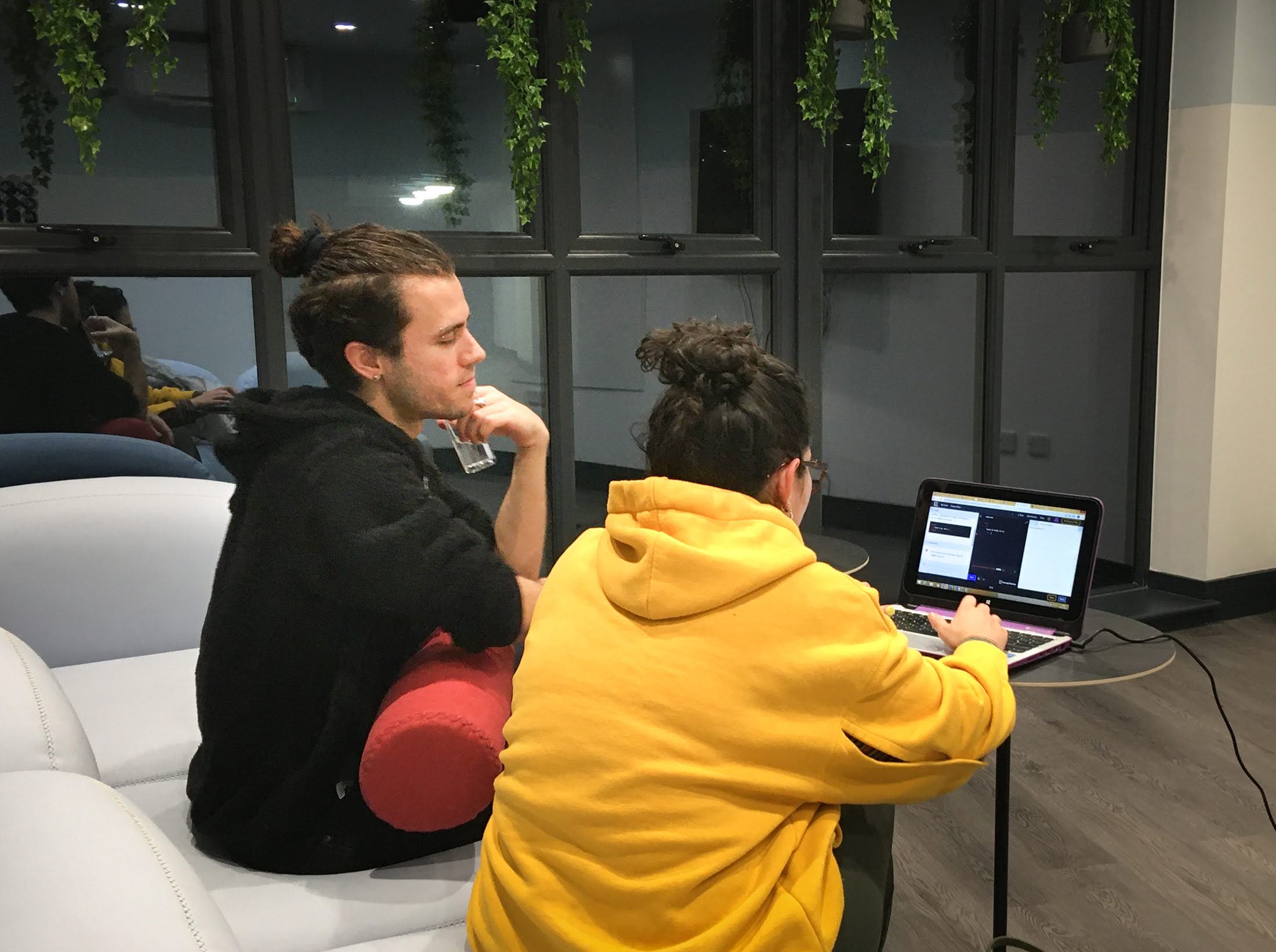 Two people with their backs to the camera sitting at a desk looking at a laptop,  attending a MPB and codebar event in Brighton. 