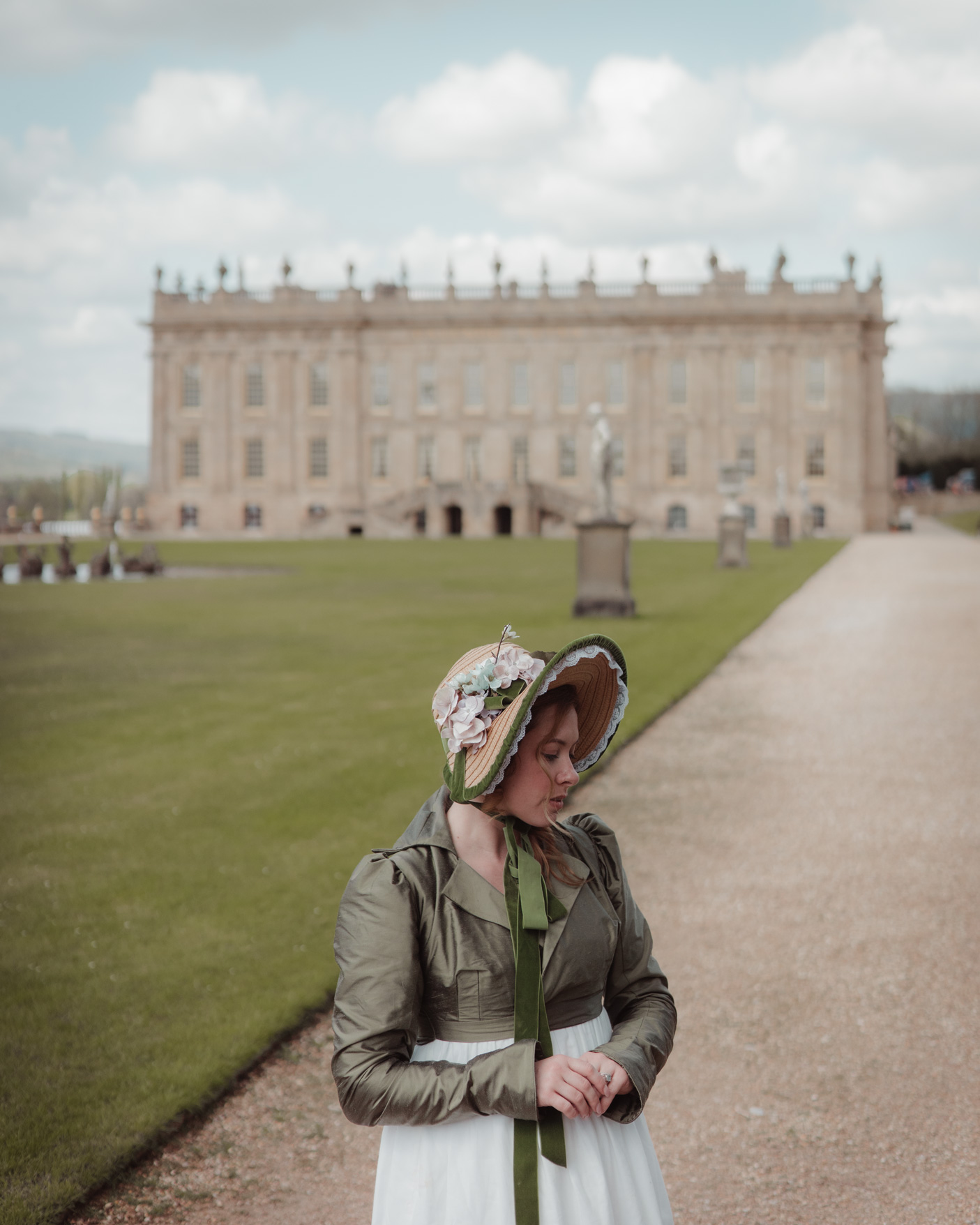 Model wearing a dark green dress and a hat poses in front of Chatsworth House in Derbyshire, UK, photo by Liza Roberts with a Canon EOS R6