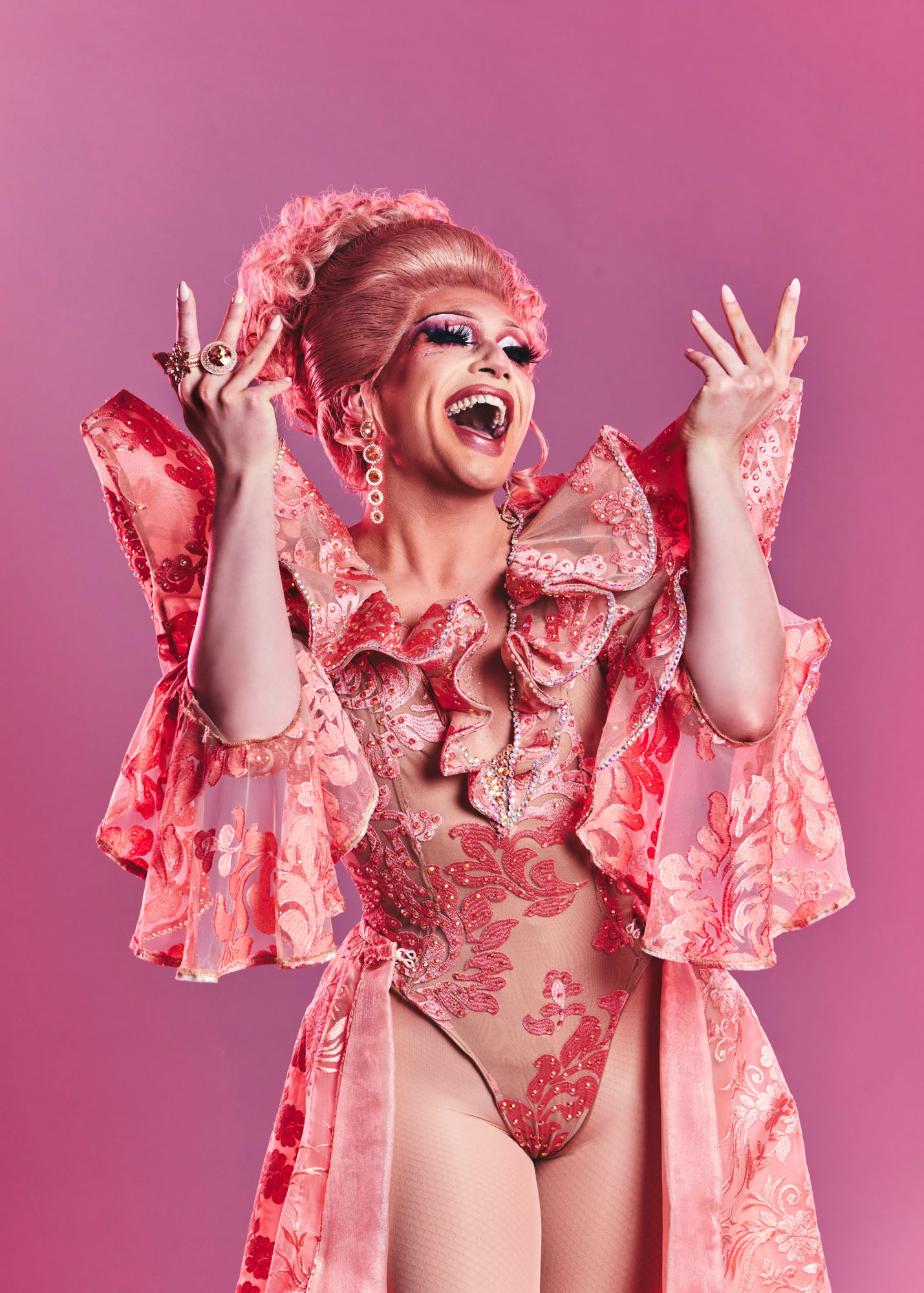 Portrait of a drag performer wearing a pink outfit, hair and rings, looking joyous