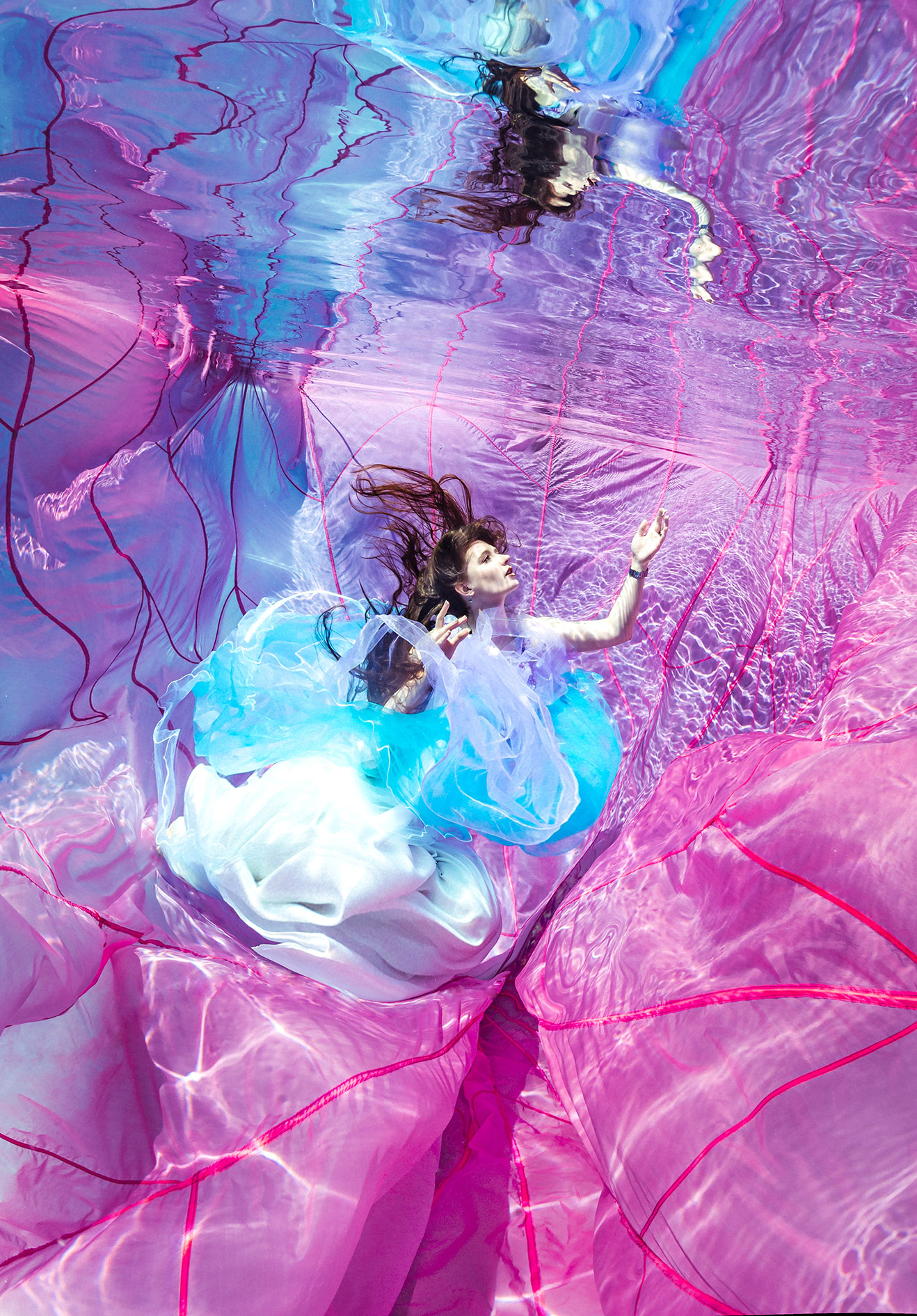 Unterwasserbild von einer dunkelhaarigen Frau die ein pinkes kleid an hat.
Spiegelung und das Spiel mit dem Licht und Schatten
Erst die Wasserspiegelung und besondere Belichtung machen das Foto so anders. Eine frontale Beleuchtung soll grundsätzlich vermieden werden.