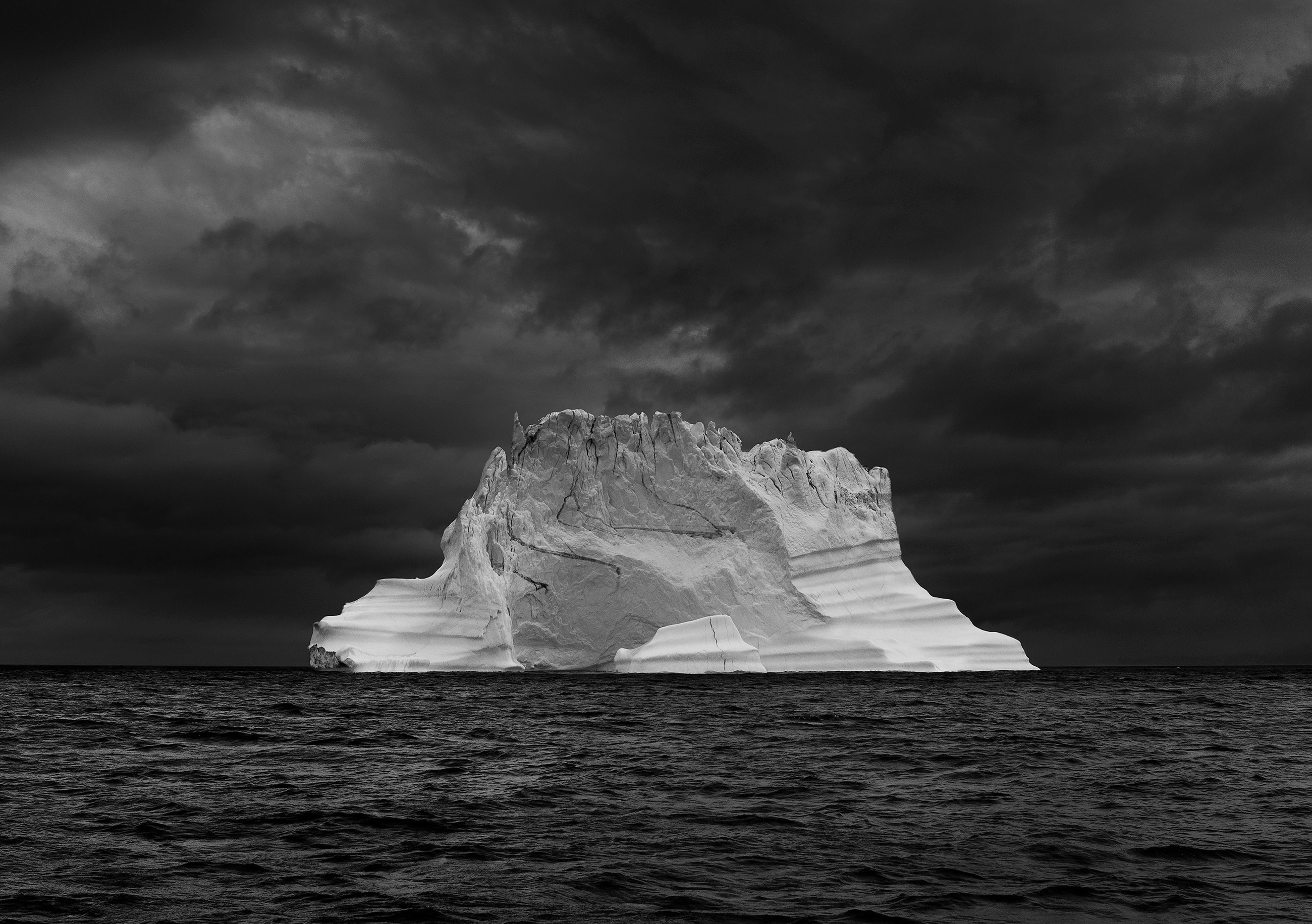 Black and white image of an iceberg in the sea, cloudy sky, photo taken by Ragnar Axelsson