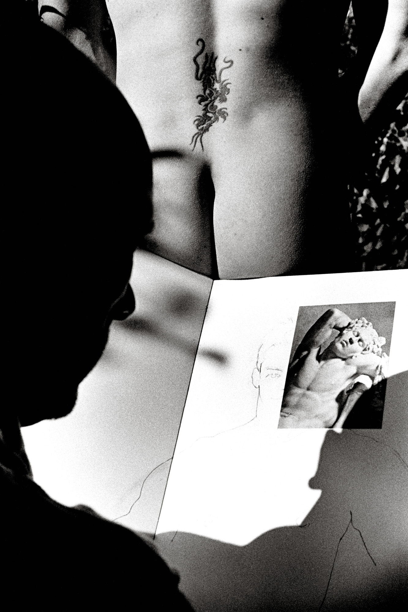 Foto en blanco y negro de un hombre mirando la imagen de una escultura y otra persona posando desnuda, de Ralph Gibson usando una Leica.