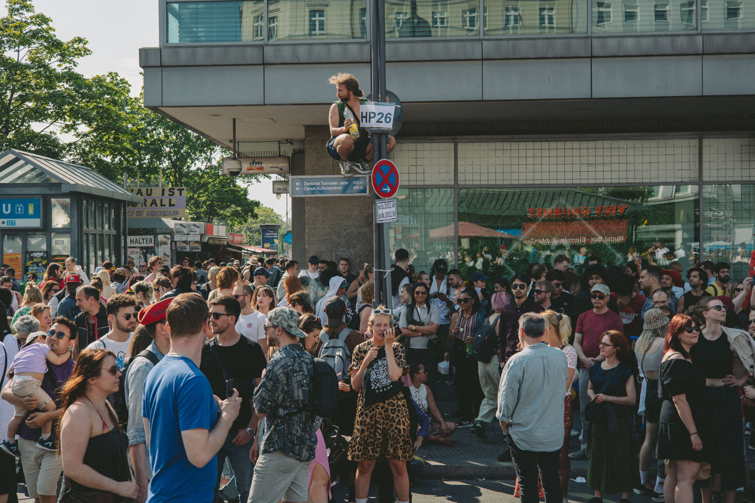Person squatting on a street sign, crowd below, shot by Stefanie Schmid Rincon with the Canon EOS R6.