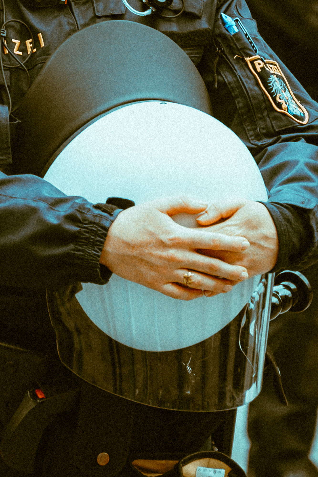 Nahaufnahme eines Wiener Polizisten, der mit beiden Händen einen weißen Helm vor seinem Oberkörper hält. Der Kontrast zwischen dem weißen Helm und der dunkelgrünen Uniform sorgt für eine kontrastreiche Farbwirkung und der enge Bildausschnitt verleiht dem Motiv eine dokumentarische Wirkung. Aufgenommen von Dhan Limwattana mit einer Nikon Z5 II.