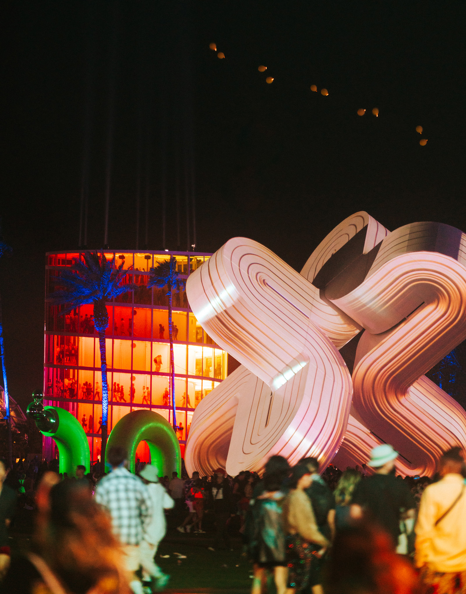 Photo of the grounds at 2023 Coachella Valley Music and Arts Festival including lighted artwork on display and crowd walking.