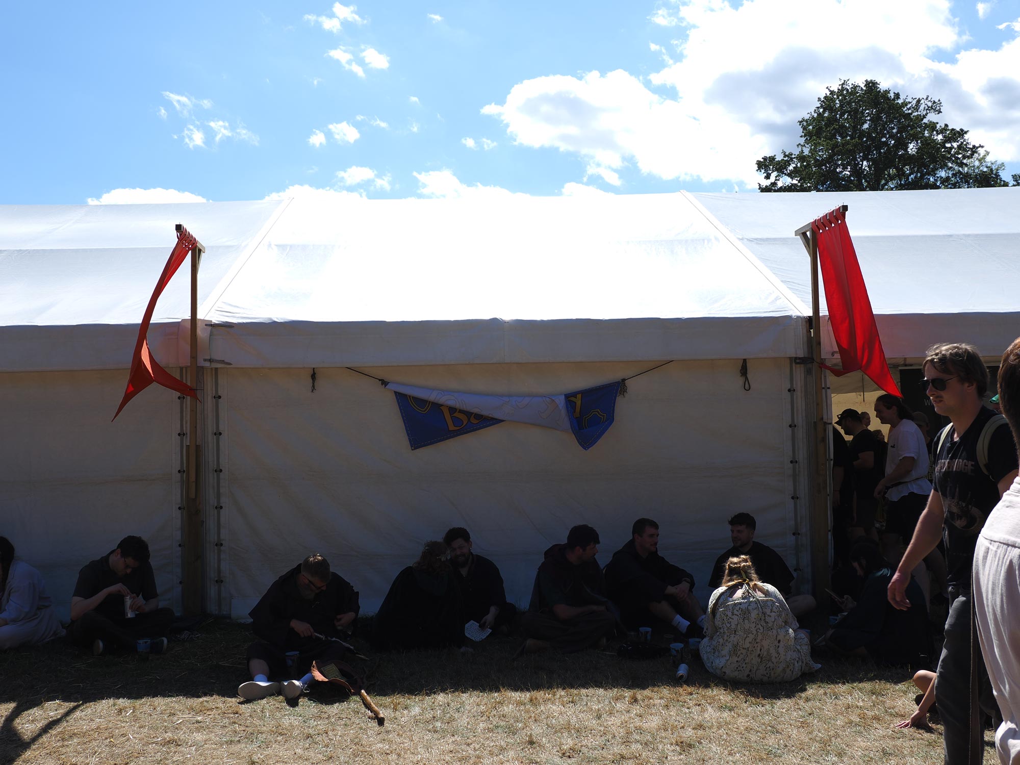 Mensen zitten in de schaduw van een bellen-tent op een zonnige dag tijdens een middeleeuws festival.