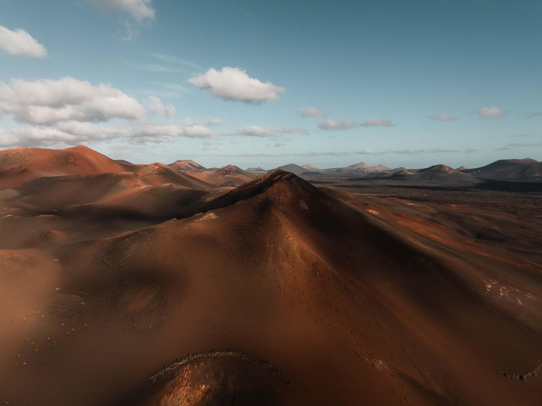 Drone aerial photo of a volcanic landscape with rolling hills and rugged terrain under clear daylight.