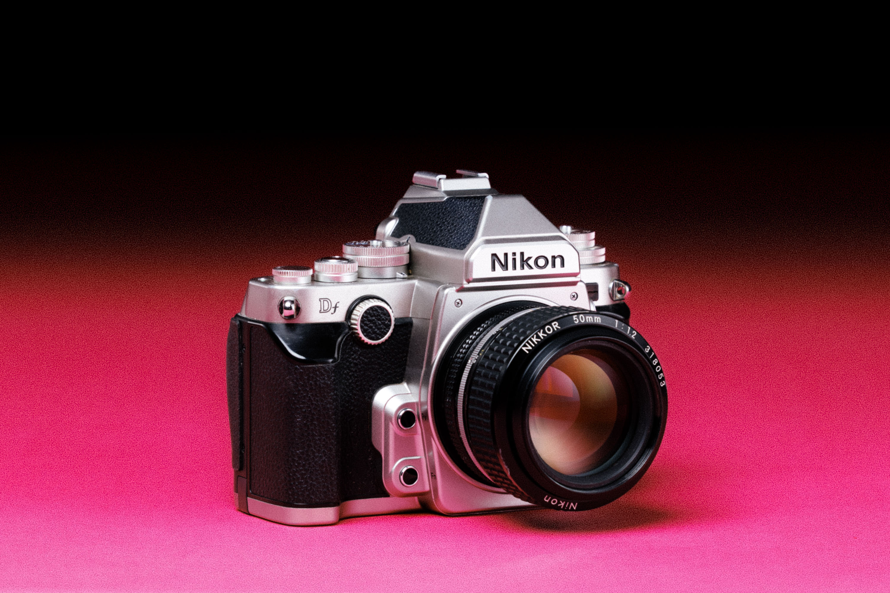 A Nikon Df with a Nikon Ai-S Nikkor 50mm f/1.2 lens, with an added film-like grain effect on a graduated pink background. 
