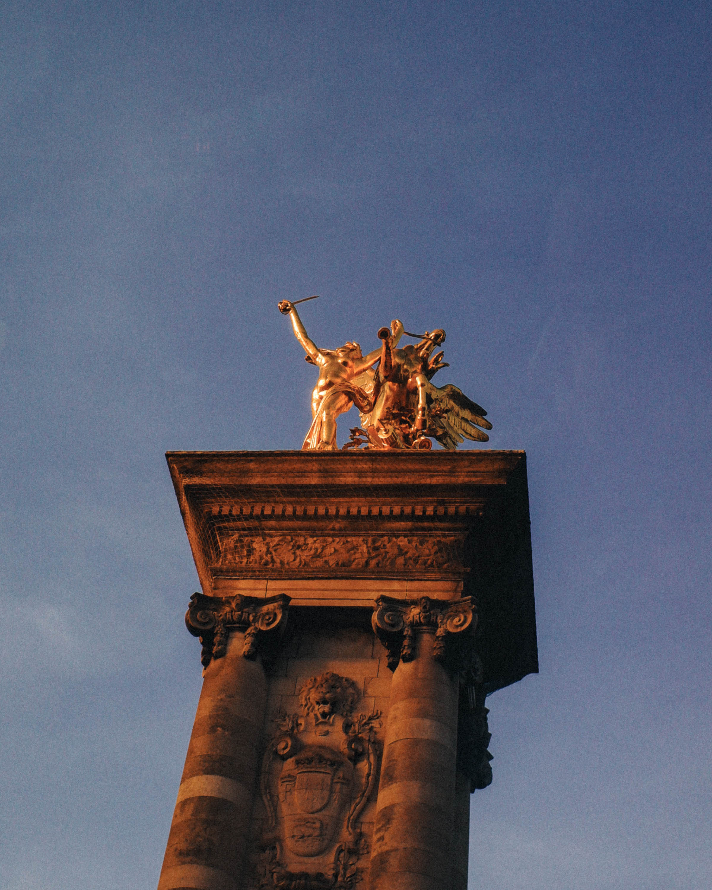 A close-up look at the golden Pegasus statue on Pont Alexandre III, illuminated by sunset against a deep blue Parisian sky.