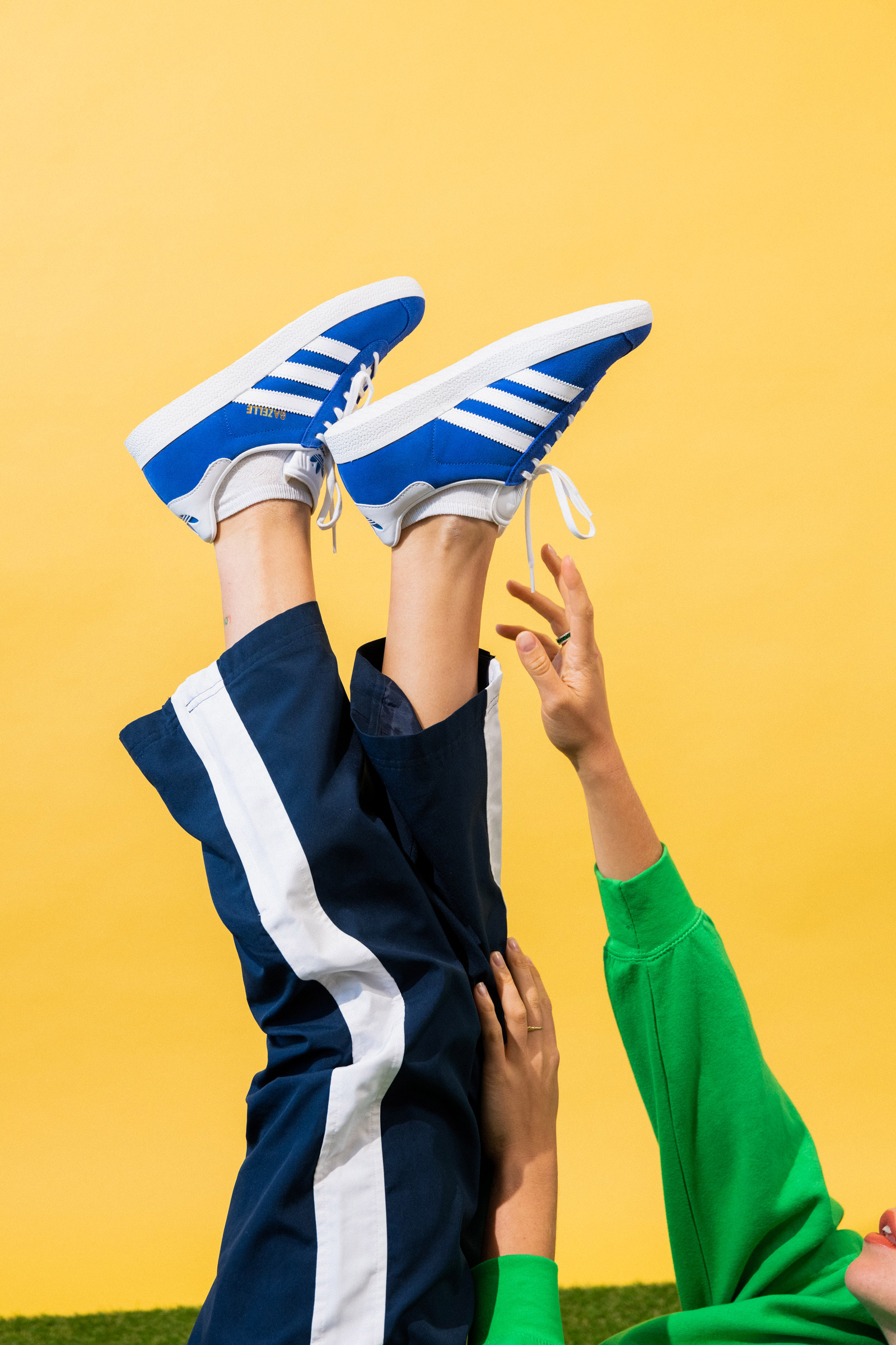 Image d'une personne avec les jambes en l'air et des chaussures Adidas bleues à bandes blanches.