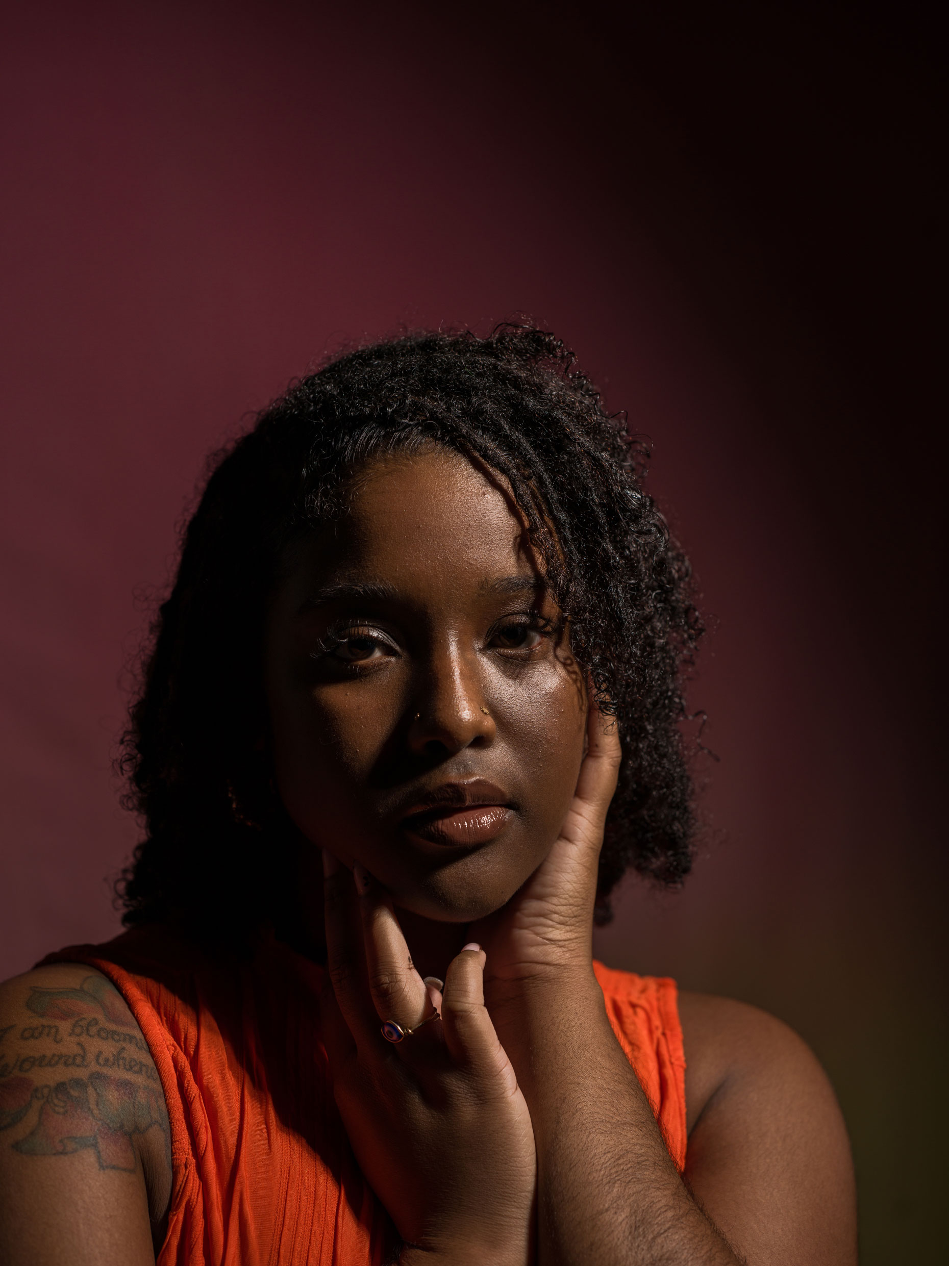 Portrait of a person with curly black hair and orange top Rembrandt lighting. Taken by Kaylah Sambo on a Hasselblad X1D-50c.