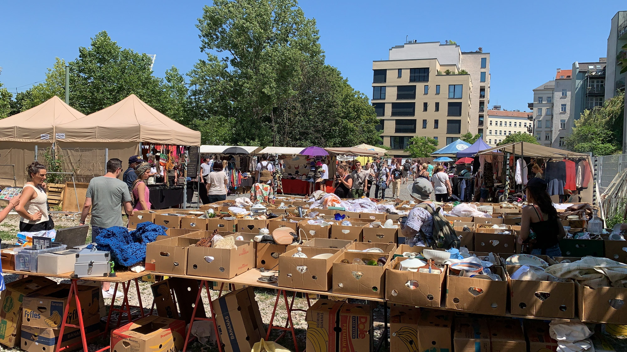 Photograph of a busy Berlin flea market on a sunny day, with shoppers browsing cardboard boxes, vintage goods and clothing stalls. Shot by Wesley Verhoeve on an iPhone XS Max.