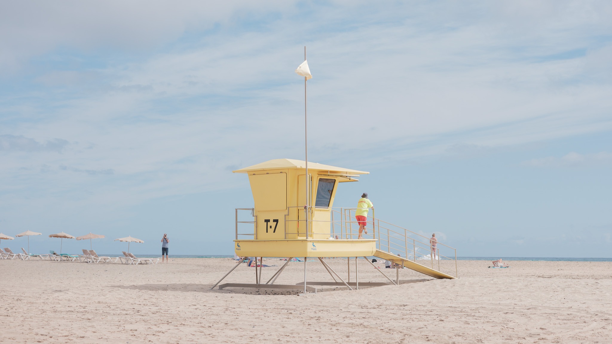 Een gele strandwachthut op het strand met een strandwacht die uitkijkt over zee, gefotografeerd door Connor Redmond.