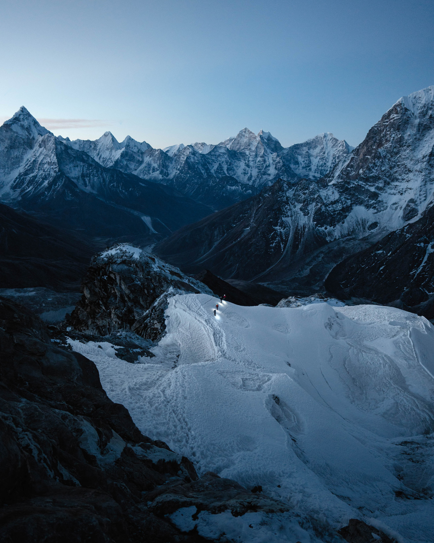 Four people wearing torches on their helmets trekking across a snow covered mountain peak with a mountain range in the background, shot by Jack Anstey with the Sony Alpha A7 IV and the Sony FE 24mm f/1.4 GM.