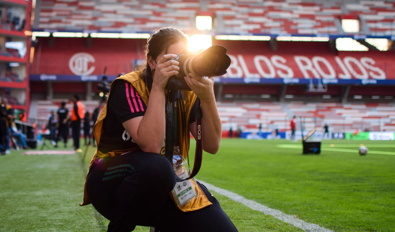 
Eliosa Sanchez kneeling while taking a photo at a football stadium


