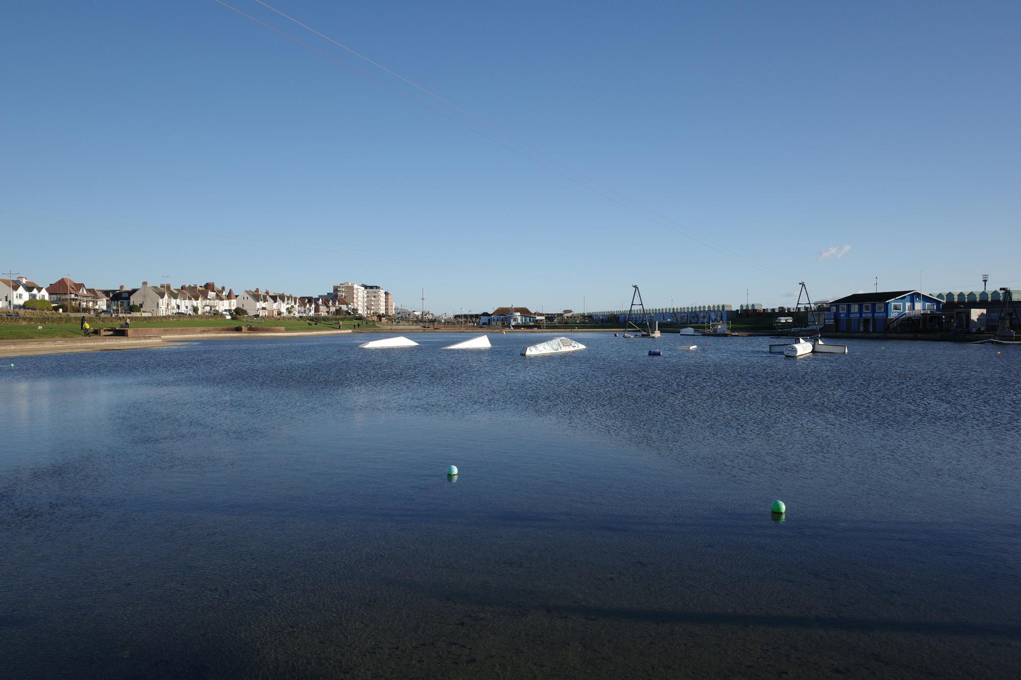Een watersportcentrum met een groot stuk water, huizen in de verte en een helderblauwe lucht boven. Geen simulatiefilter gebruikt.