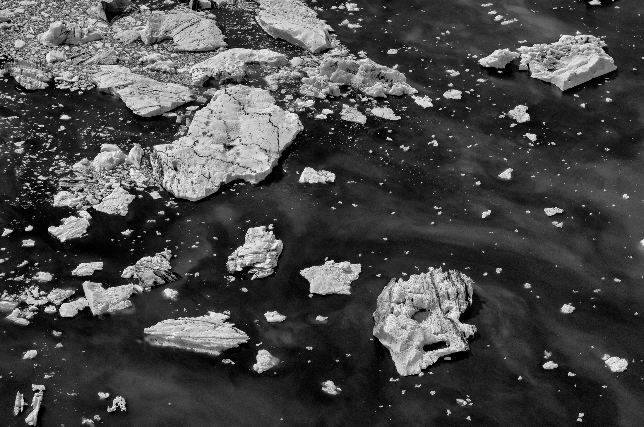 Black and white image of fragmented ice sheets floating on the sea, photographed from above, photo taken by Ragnar Axelsson