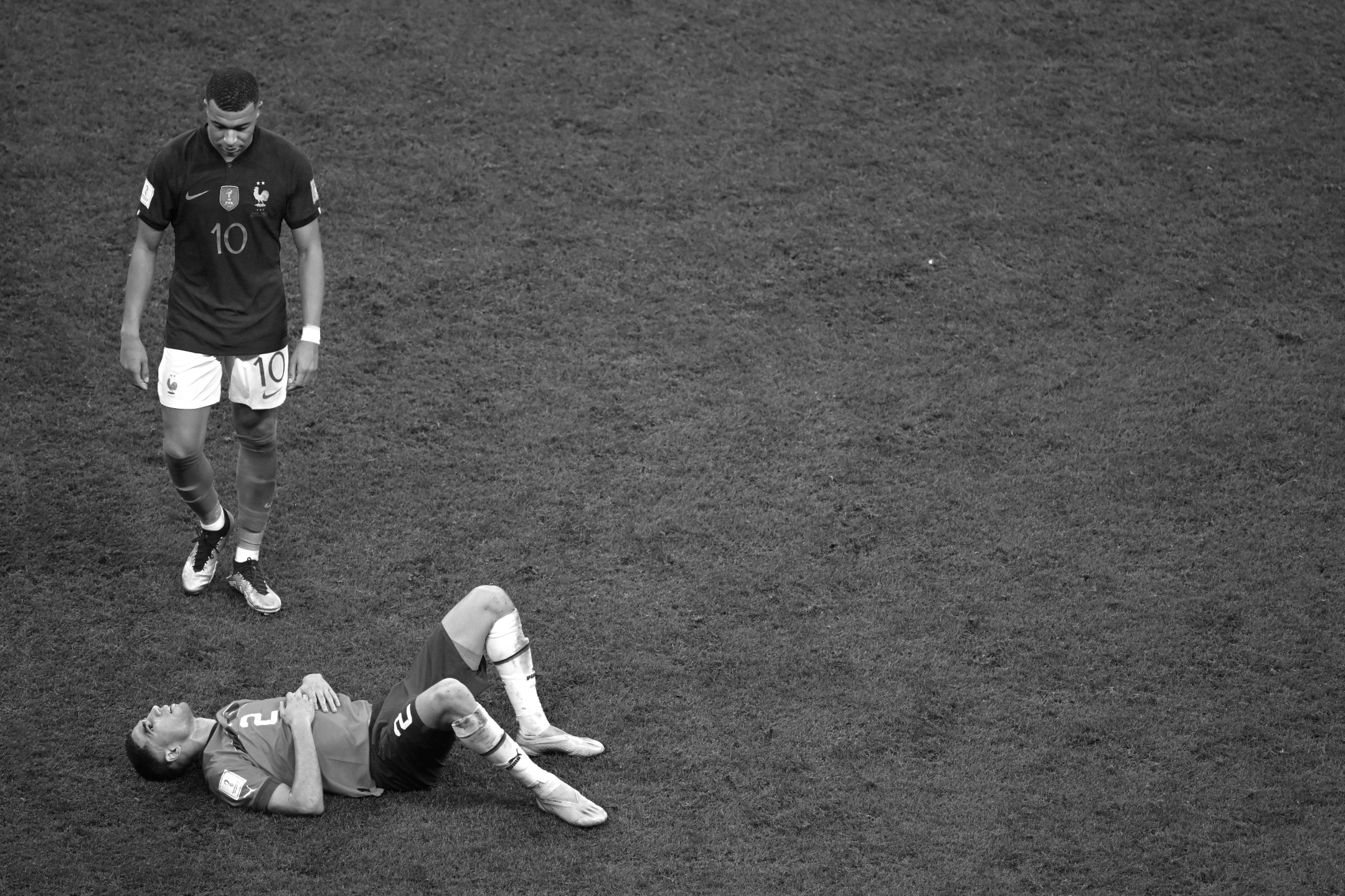 Ein Schwarz-Weiß-Foto des französischen Spielers Kylian Mbappé, der nach dem Sieg Frankreichs im Halbfinale der Fußball-Weltmeisterschaft 2022 an dem am Boden liegenden marokkanischen Spieler Achraf Hakim vorbeigeht, aufgenommen mit einer Nikon Z9 von Ryu Voelkel.