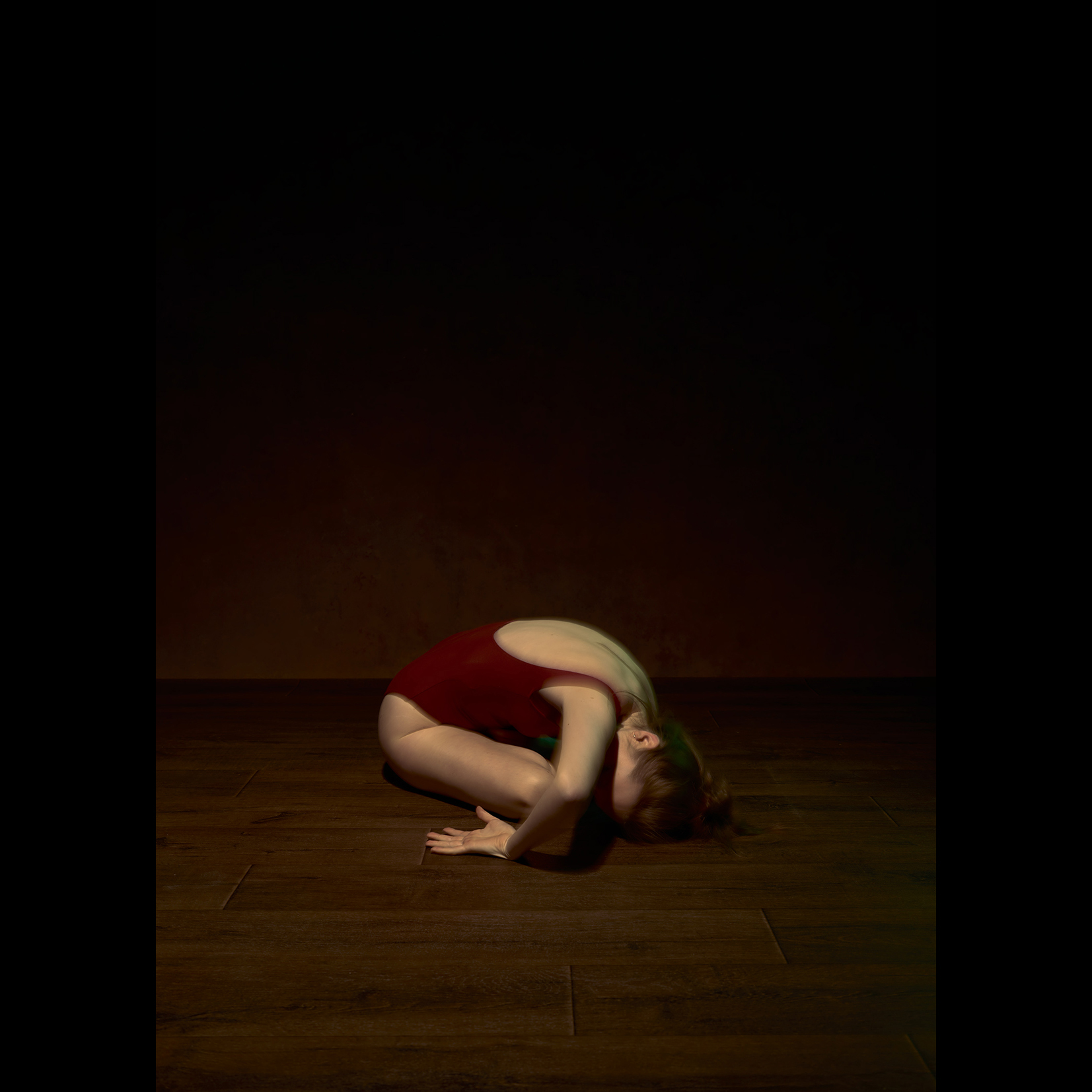 Dancer in red sitting on a wooden floor