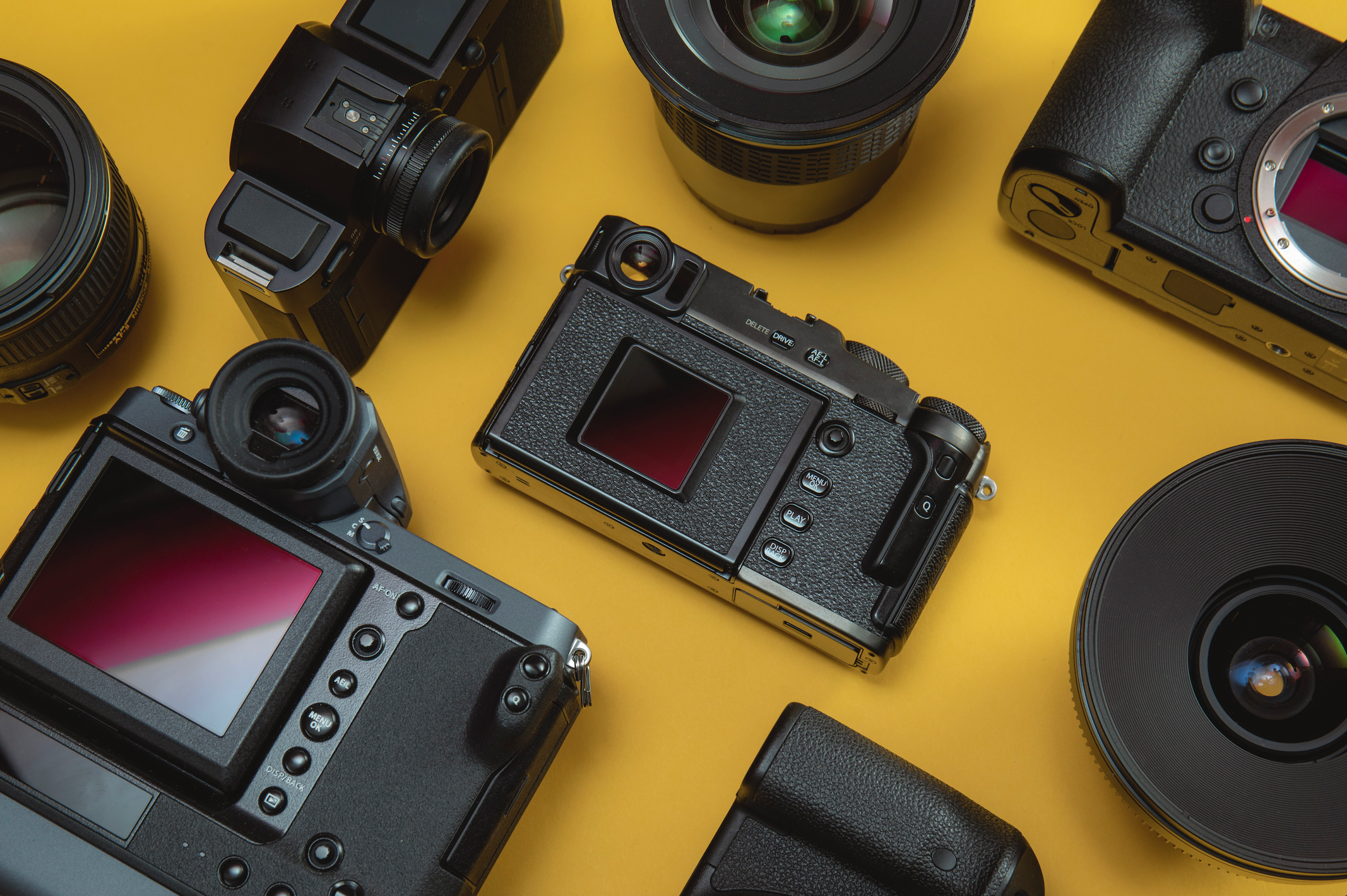A number of cameras and lenses arranged flat on a yellow background
