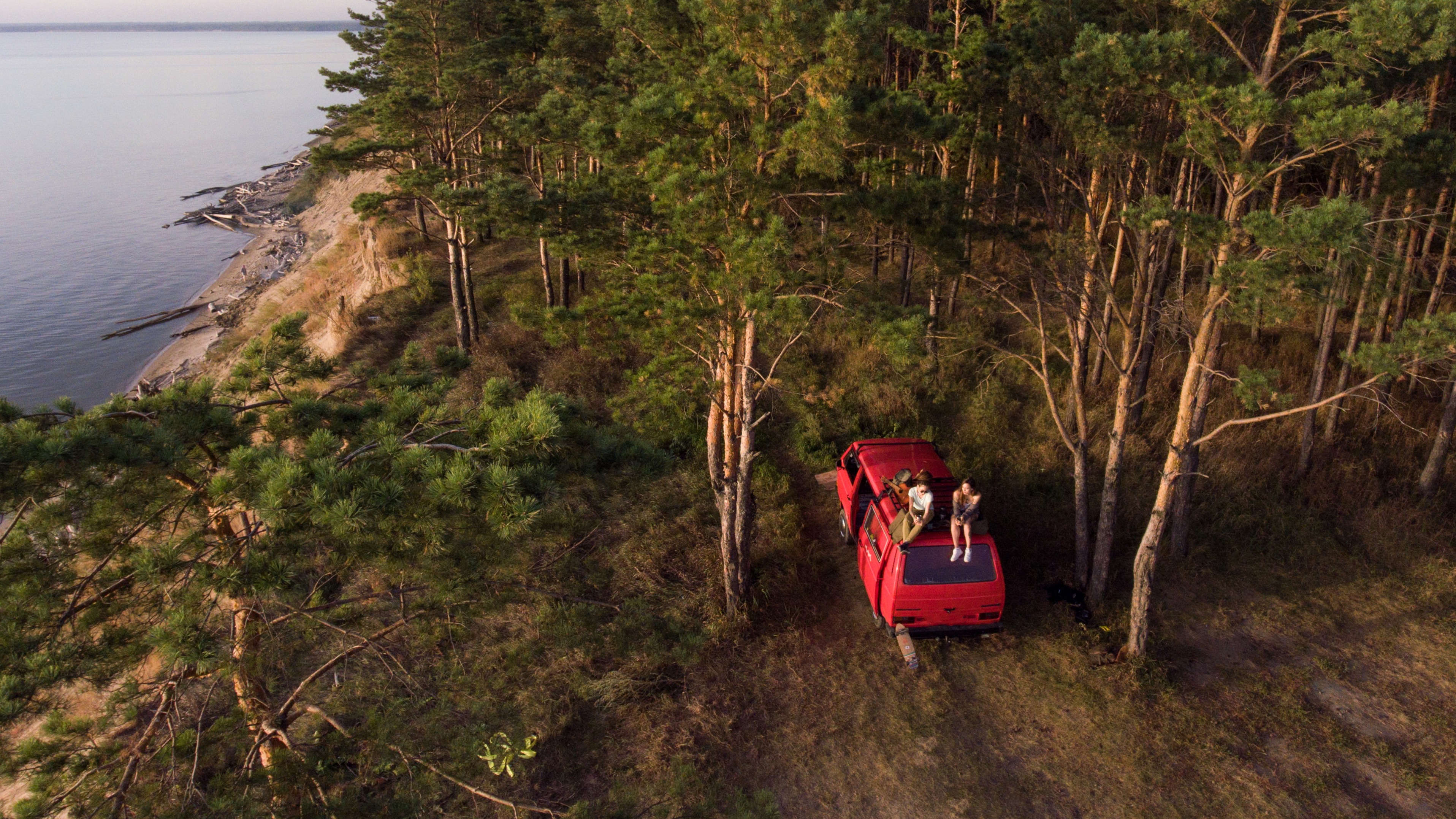 Friends sitting on top of a van on the top of a luscious mountain near an ocean.