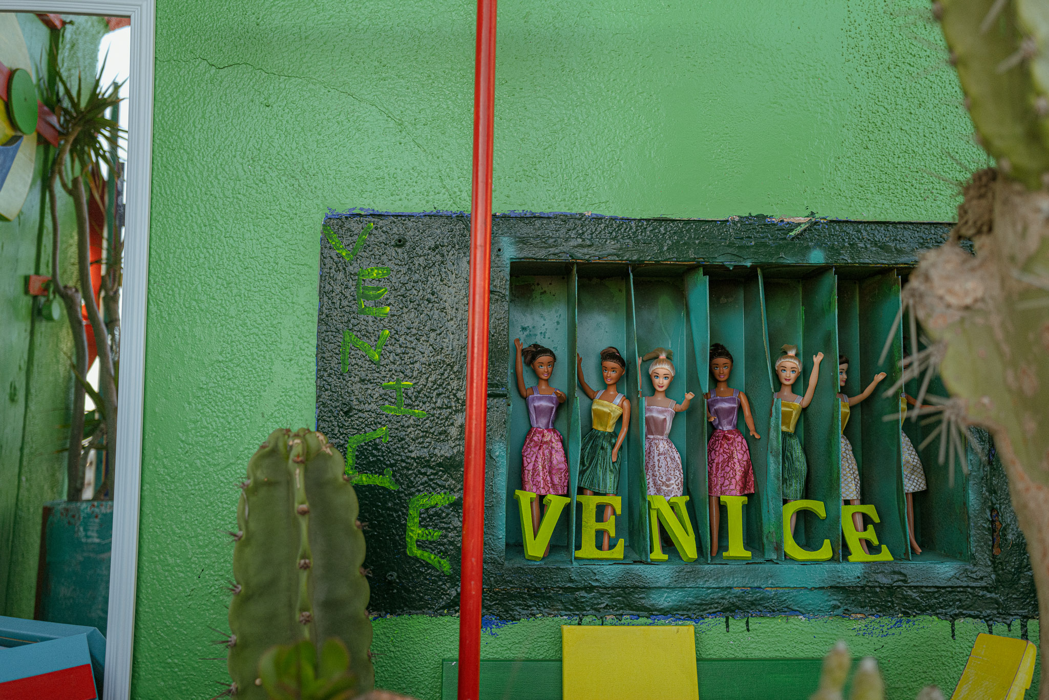 Des poupées Barbie sur un panneau mural indiquant "Venice" sur un mur vert.