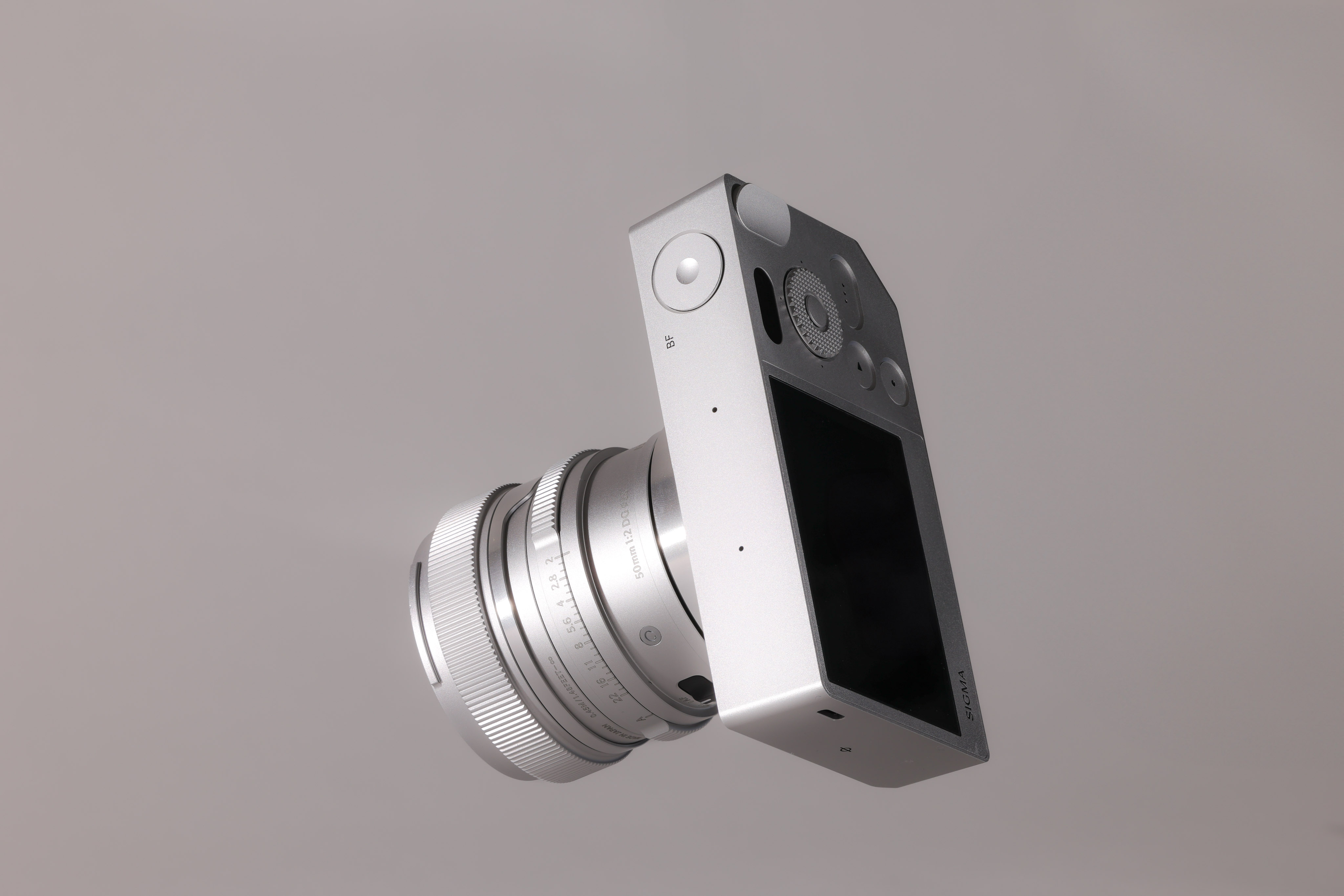 Sigma BF mit Sigma 50mm f/2 DG DN Contemporary-Objektiv, die über einem grauen Hintergrund schwebt.