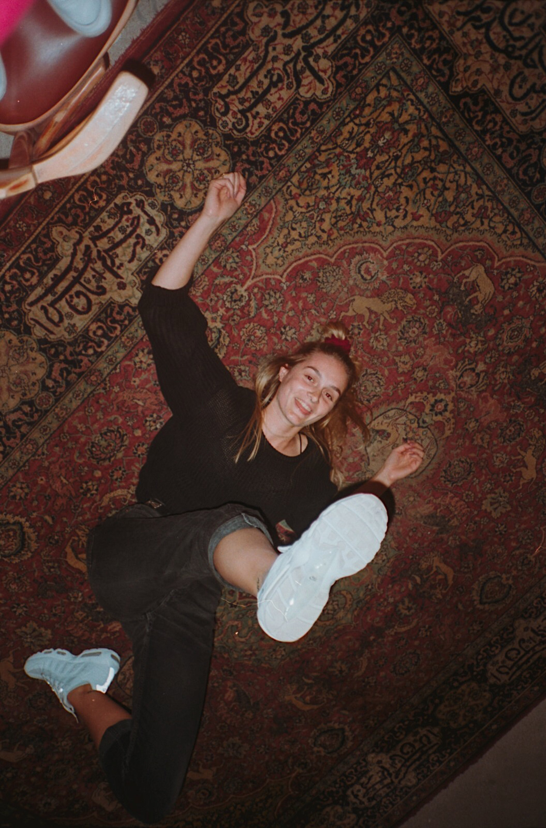 Porträt aus der Vogelperspektive einer Frau, die am Boden auf einem Teppich liegt und einen Fuß in Richtung Kamera streckt 

