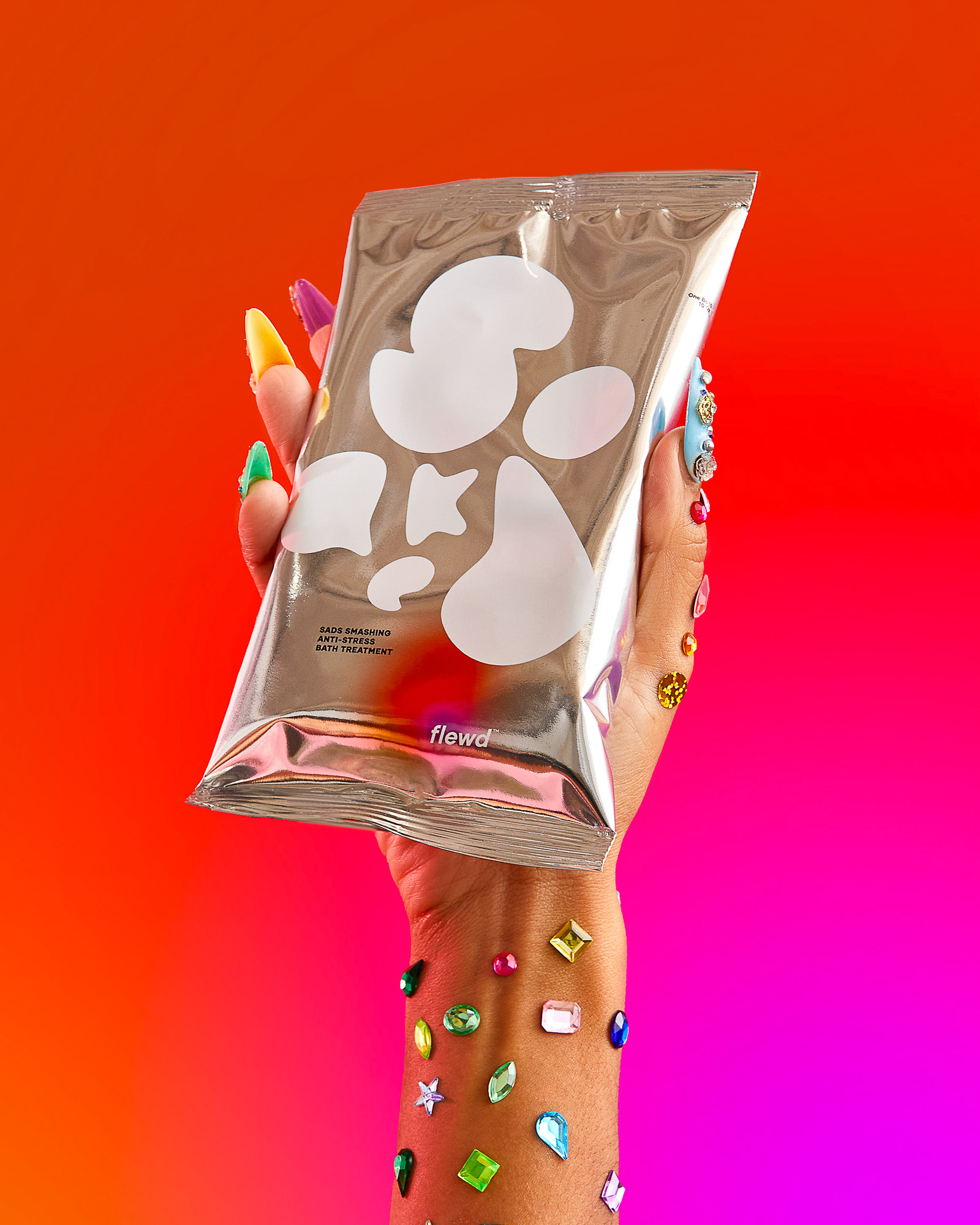 Colorful image of flewd packaging held by a hand with colorful nails and gems on the wrist.