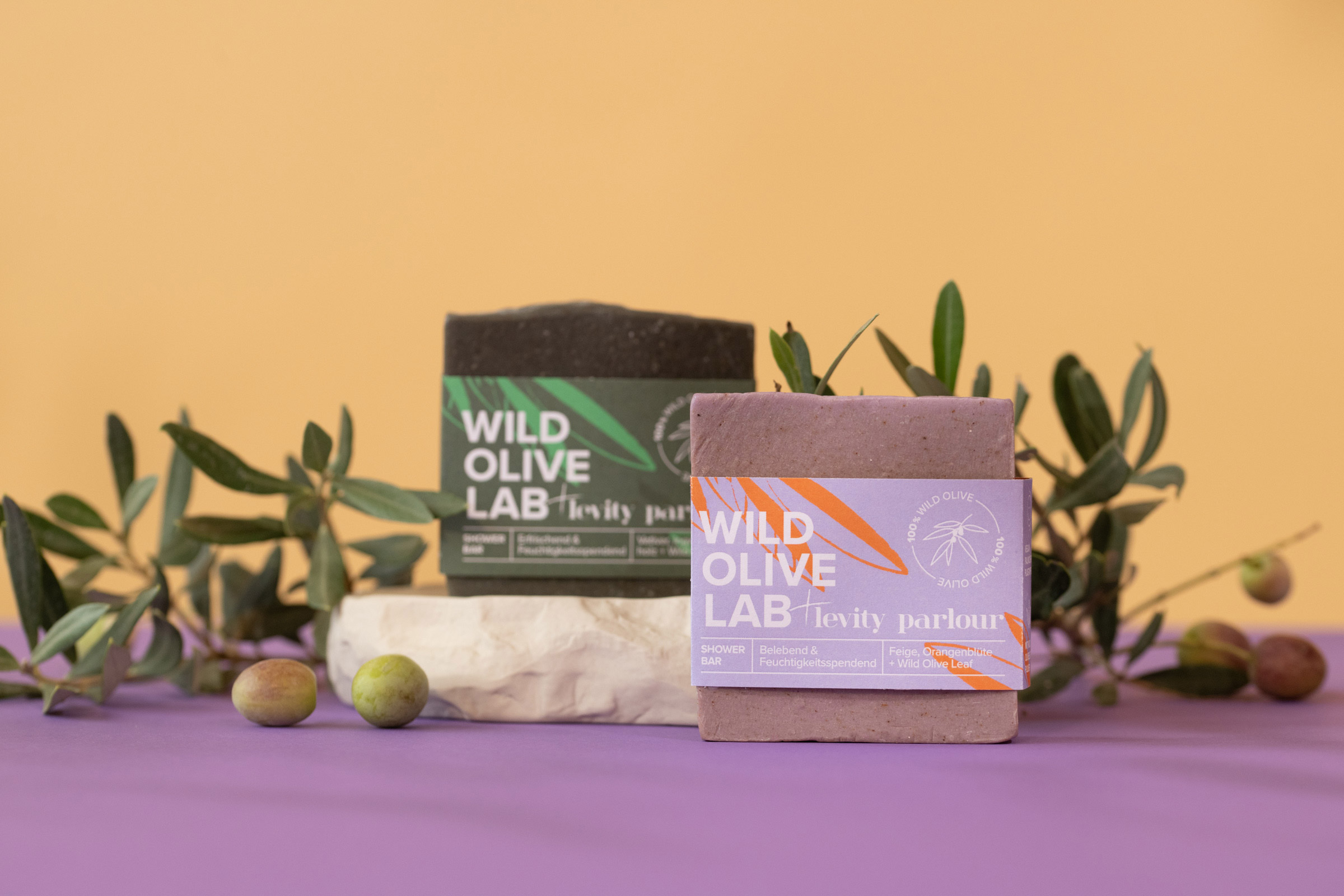 Image de deux produits de la société "WILD OLIVE LAB", drapés d'un rameau d'olivier.
