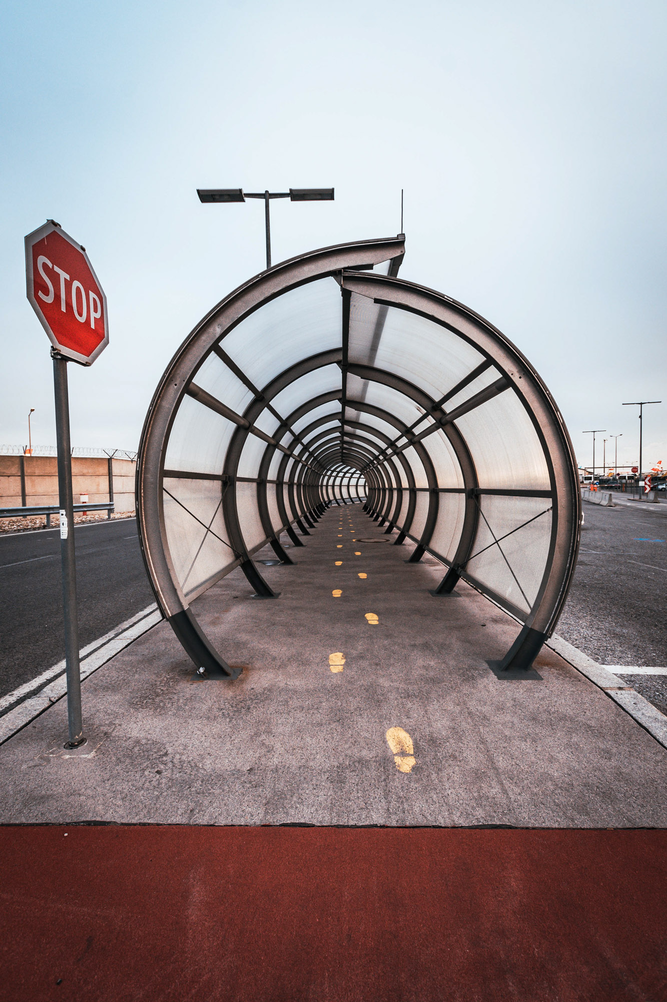 Symmetrischer, tunnelartiger Fußgängerdurchgang am Flughafen Wien mit runden Metallbögen und Fluchtlinien bis zum Ausgang. Links ein Stoppschild. Aufgenommen an einem bedeckten Tag von Dhan Limwattana.