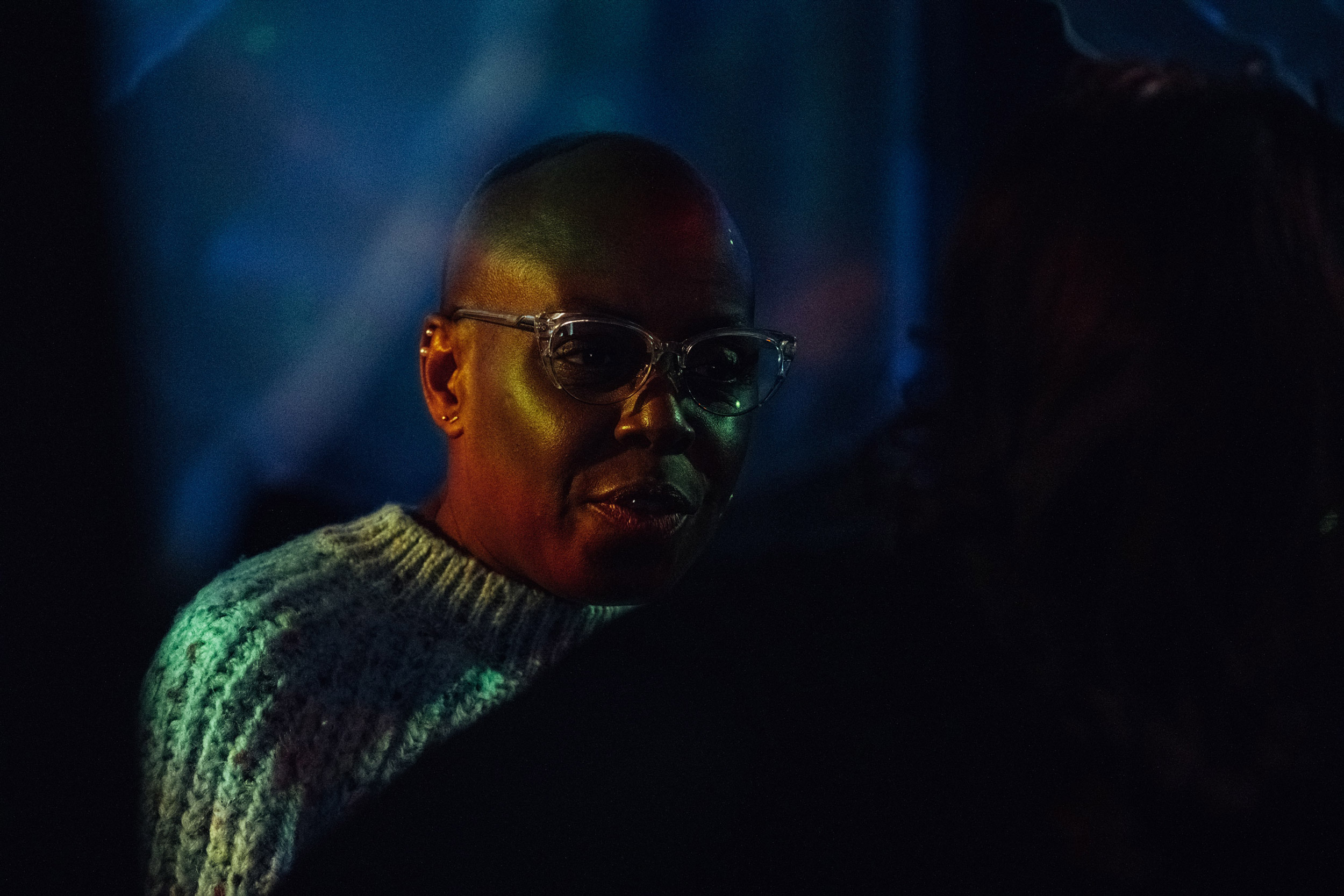 Une personne portant des lunettes et un pull blanc dans des conditions de faible luminosité. Photo prise avec un Fujifilm X-T5