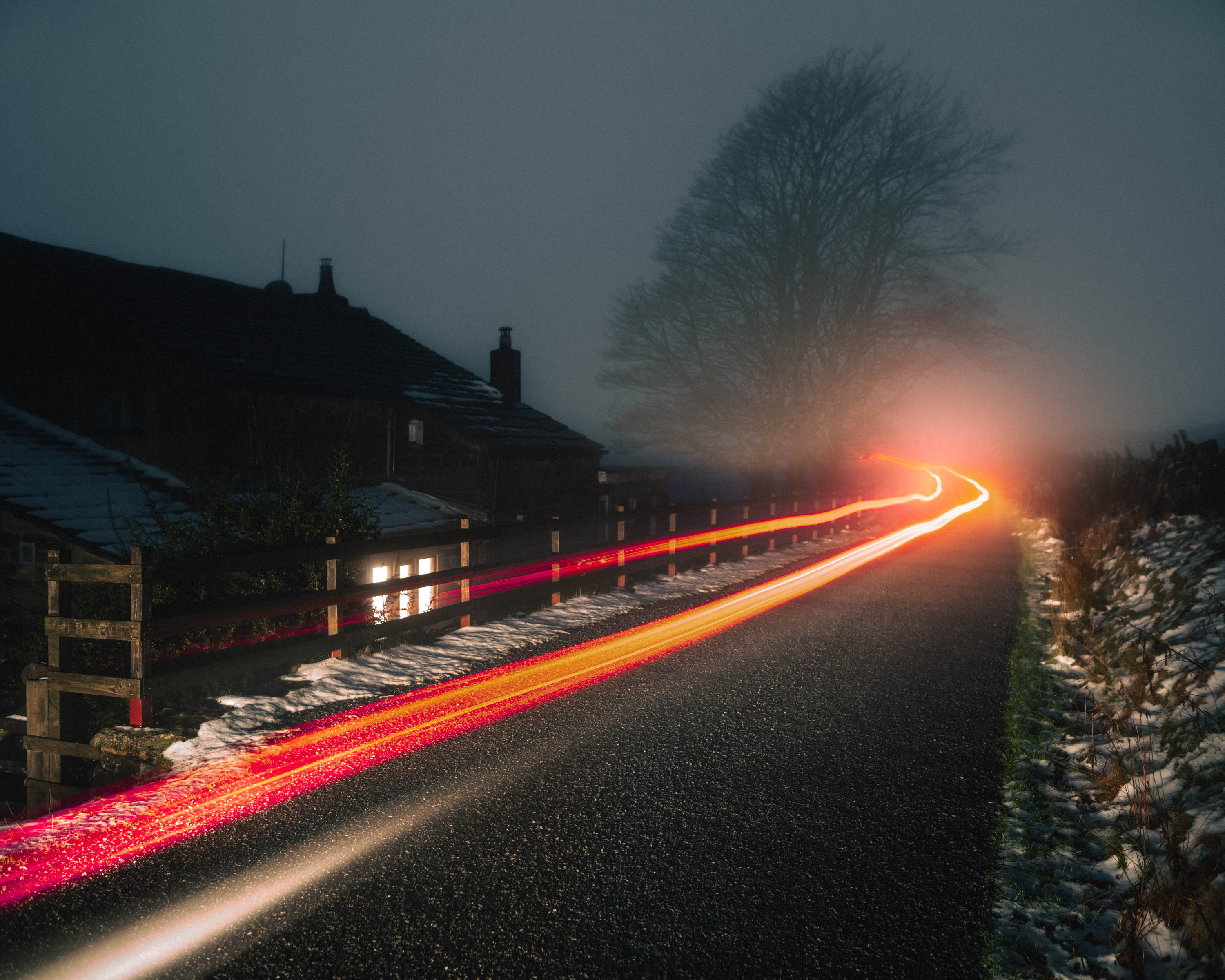 Light painting of a car passing by houses and a tree in the fog