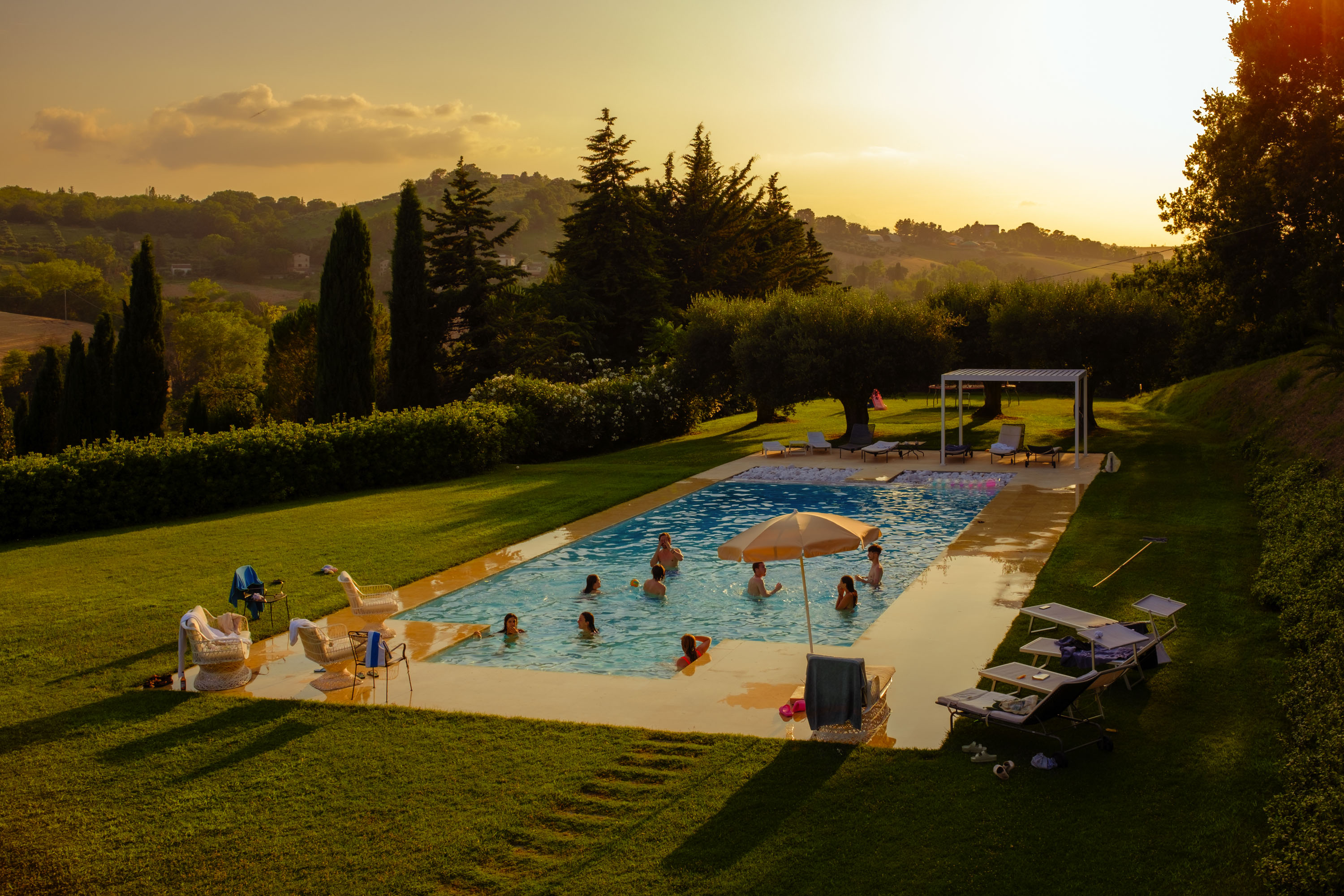 Ein Swimmingpool in einer italienischen Villa mitten im Sommer mit einer hellen, tief stehenden Sonne über dem Kopf. Von Connor Redmond.