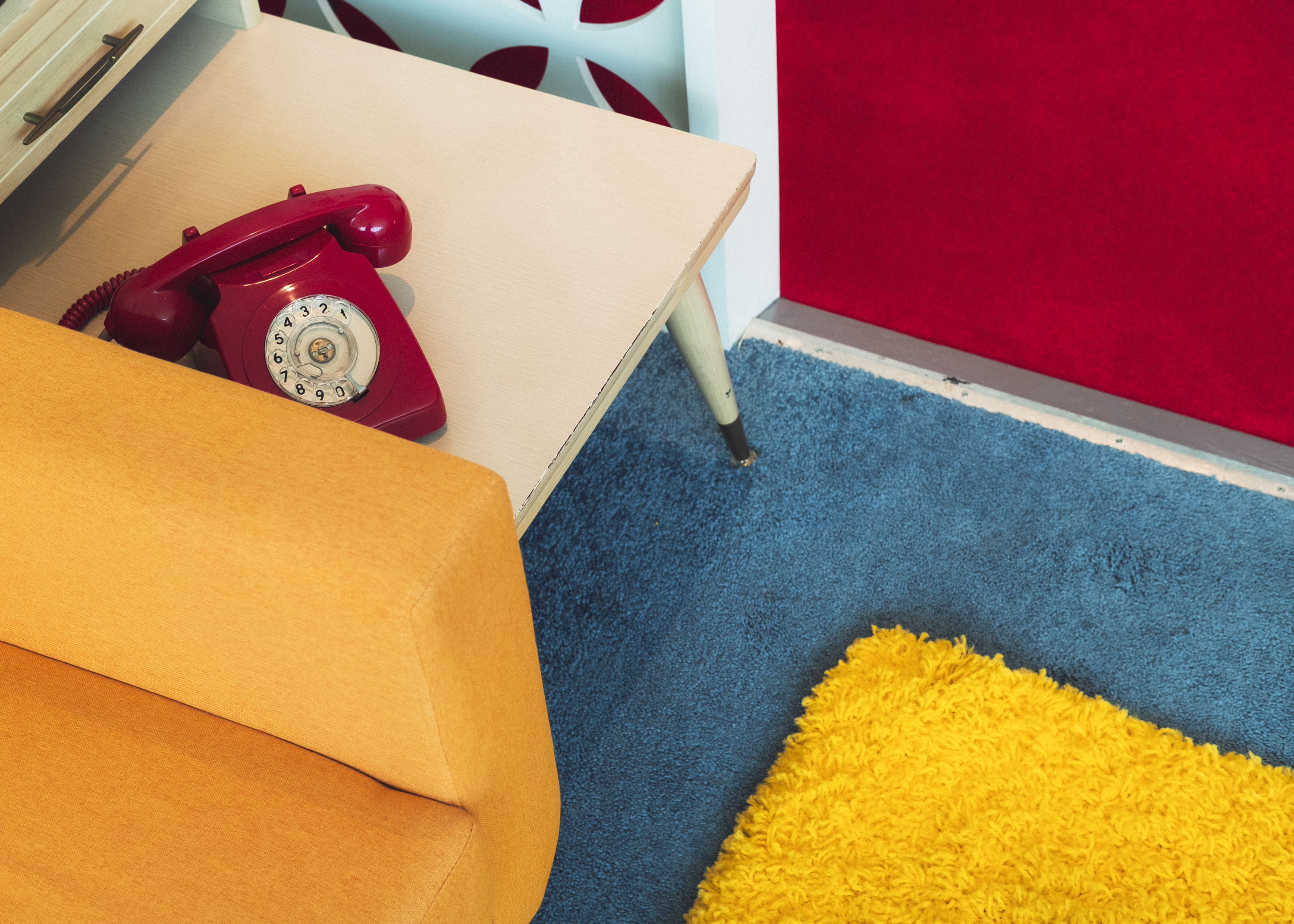Un téléphone rouge au look rétro sur une table d'appoint de style mid-century, à côté d'un canapé jaune vif. Photo prise avec le X-Pro 3 par Ian Howorth.