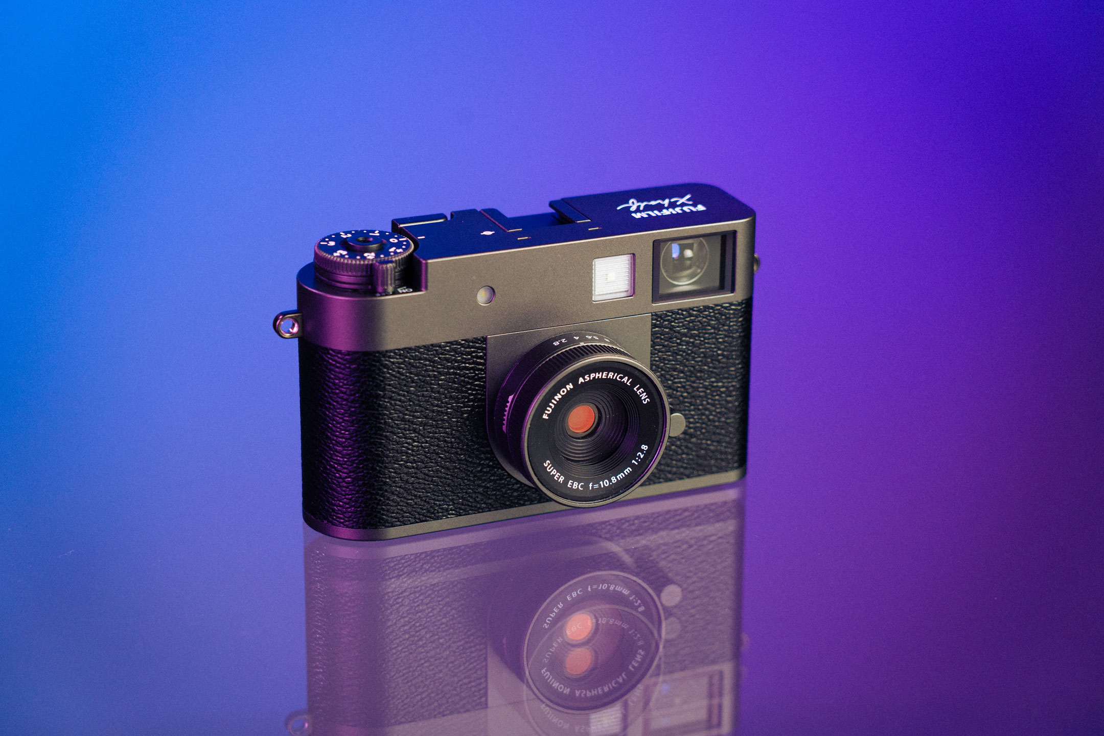 The front of the Fujifilm X half camera on a reflective surface against a purple backdrop. 