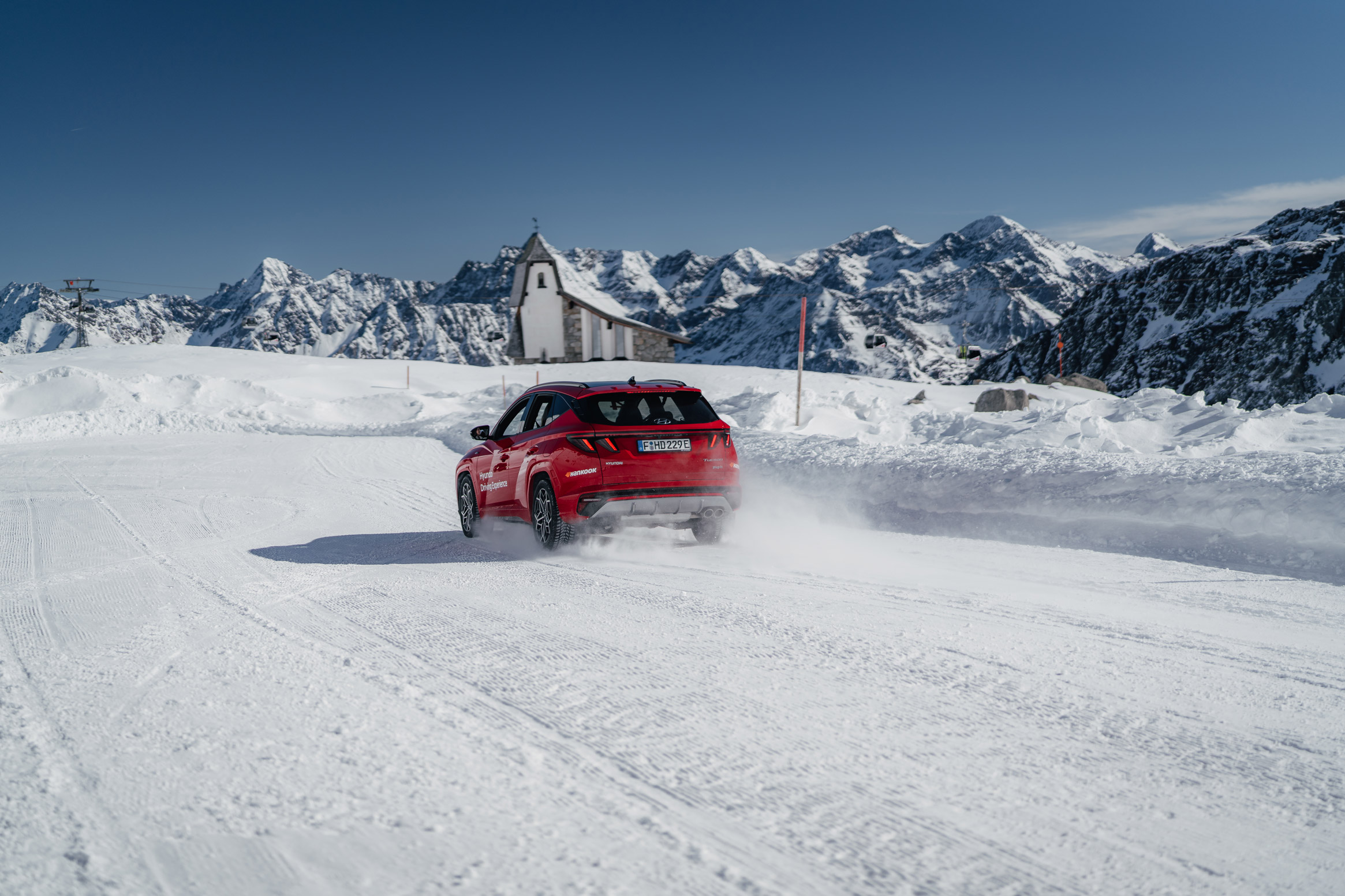 Red vehicle driving on a snowy glacier in front of mountains in Austria