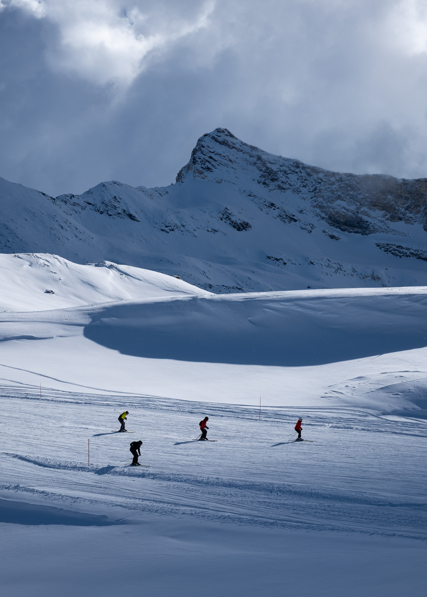 Skiiers skiing down a slope in the Alps with mountains in the background. Taken on the Fujifilm X100VI by Amy Moore.
