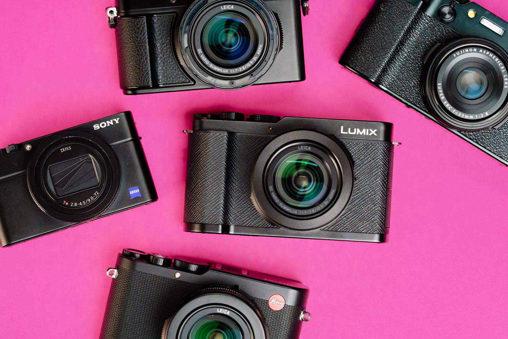 A selection of everyday carry compact cameras on a pink background. From L-R: Sony RX100 VII, Panasonic Lumix L10, Leica Q3 and Fujifilm X100VI.