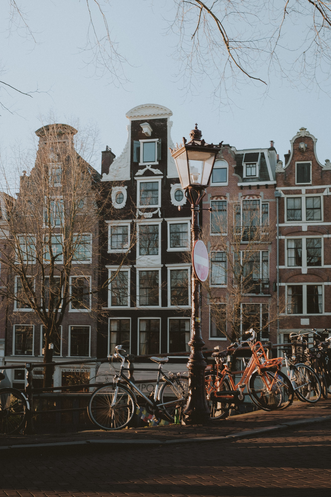 Maisons traditionnelles bordant les canaux d’Amsterdam, avec vélos stationnés et lampadaire, photographiés dans une lumière chaude de fin de journée mettant en valeur l’architecture néerlandaise et la vie urbaine