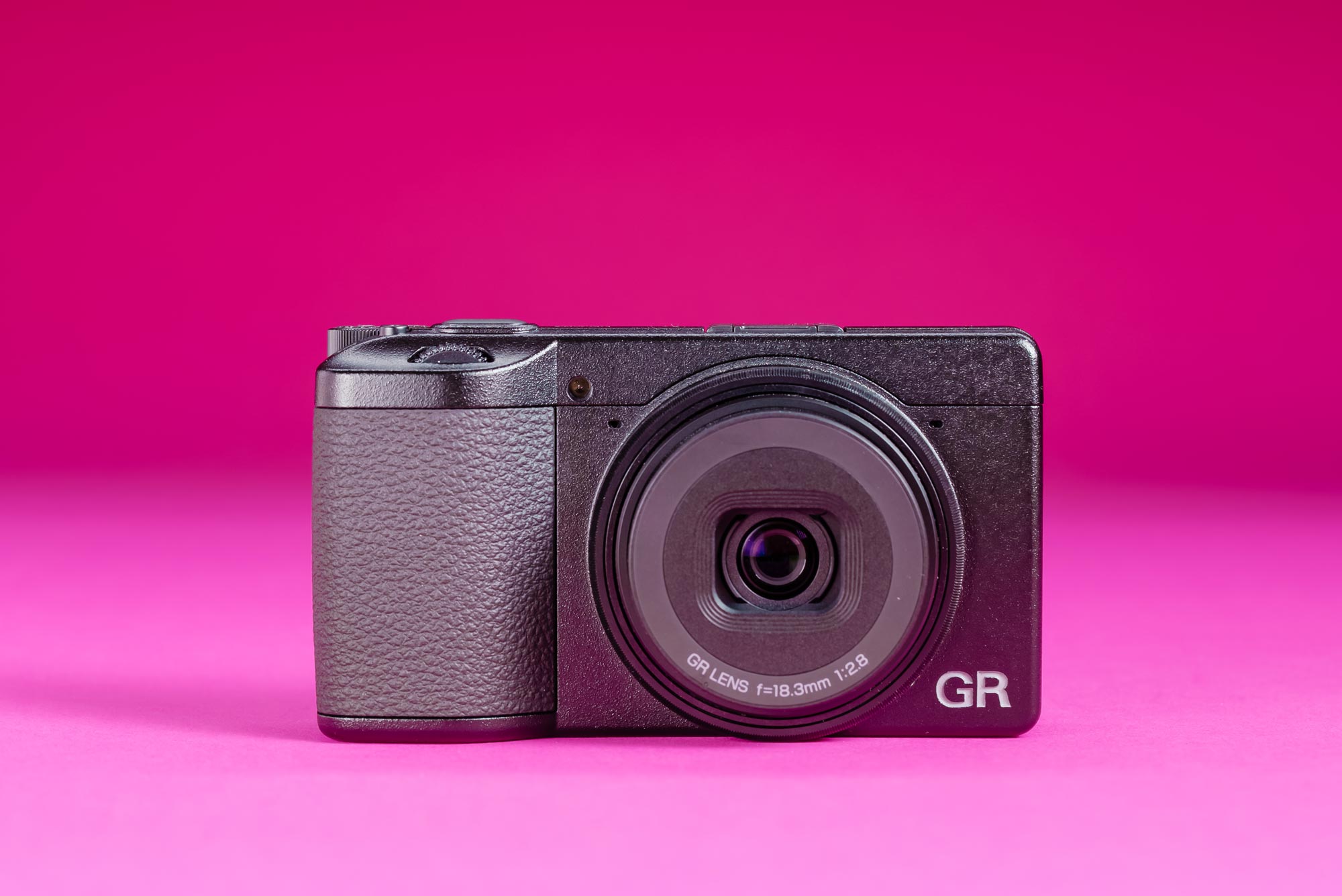 A used Ricoh GR IV on a graduated pink background.