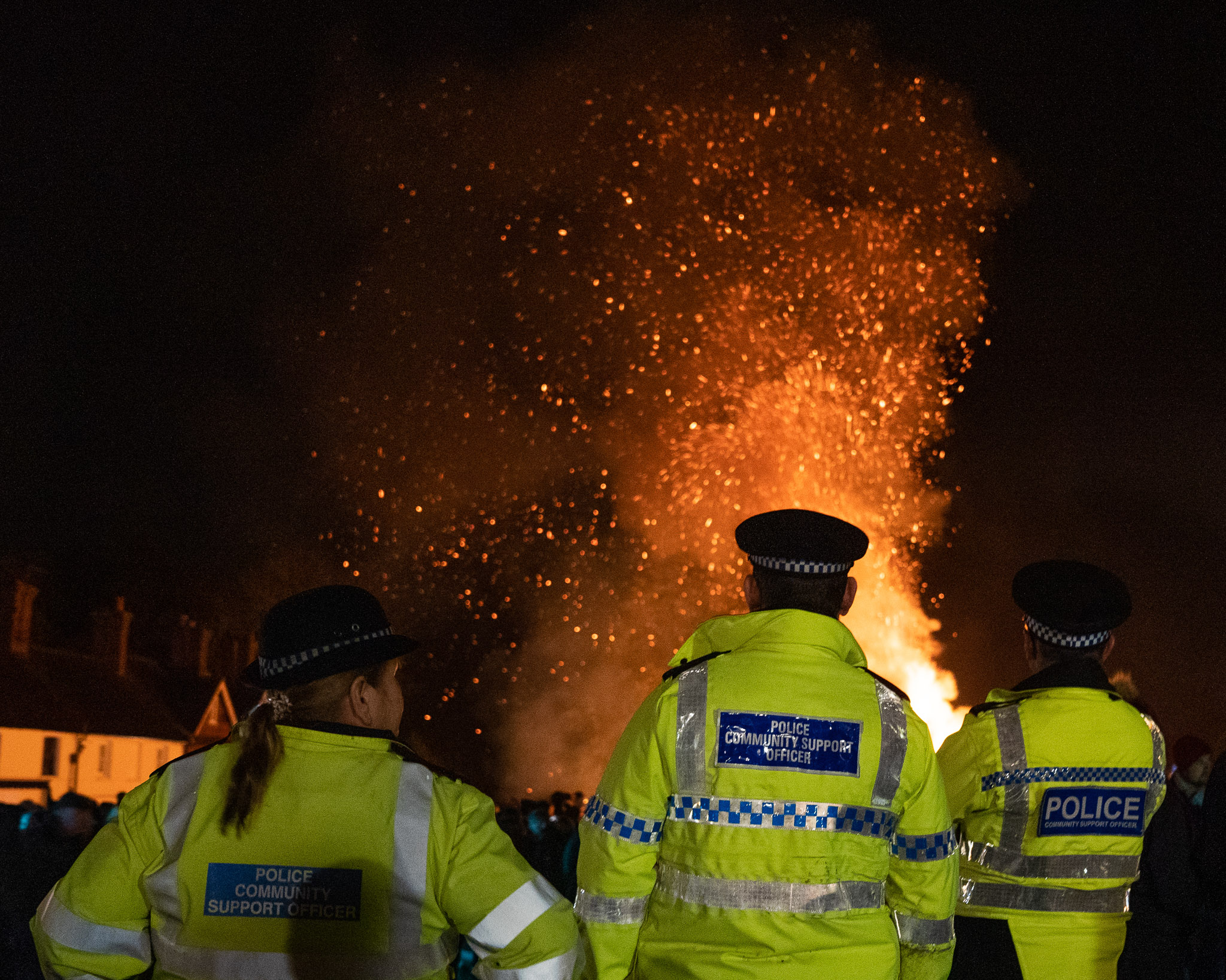 Drei britische Polizeibeamte beobachten ein Lagerfeuer, von hinten fotografiert