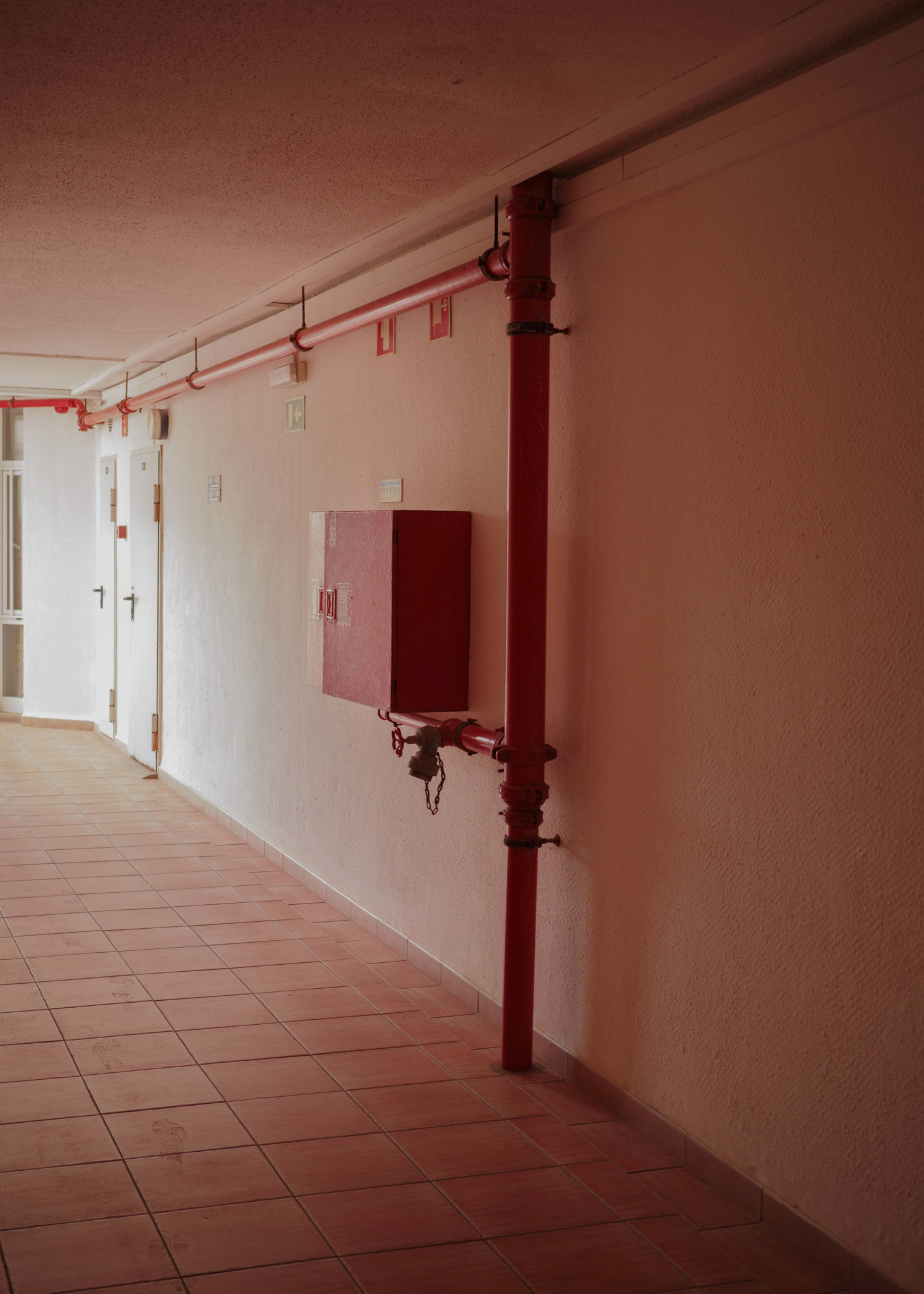 Hallway containing red water pipes attached to the wall. By Connor Redmond. 